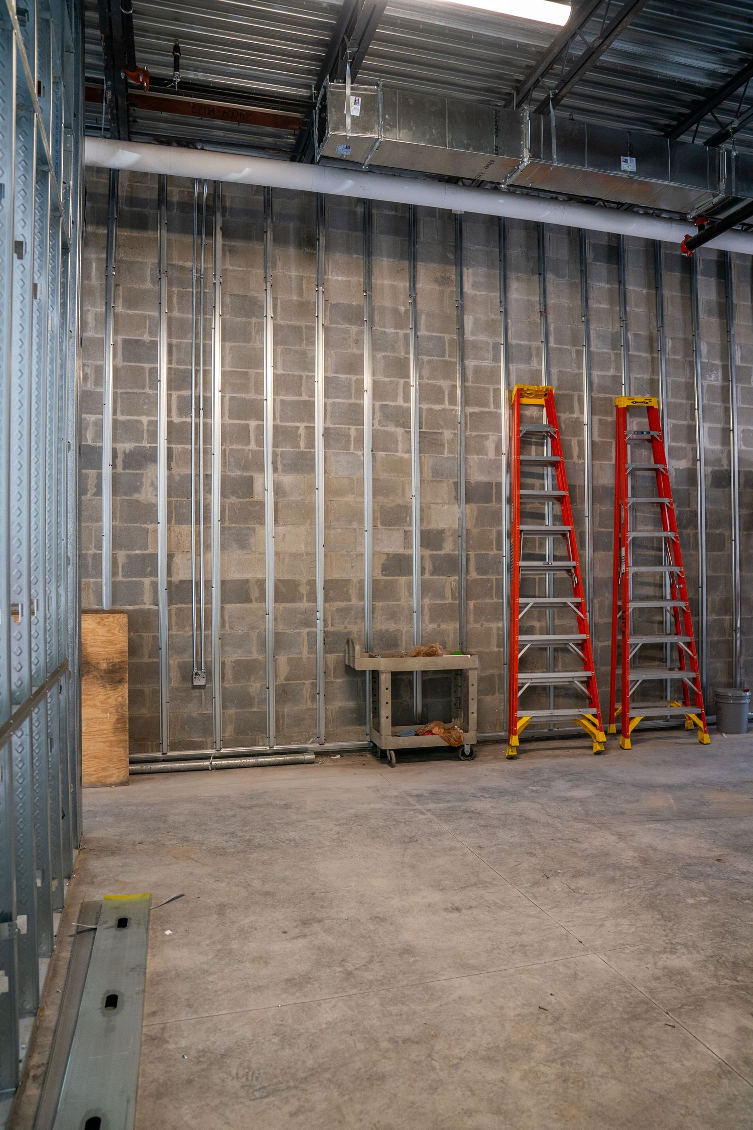 Empty commercial space under construction with red ladders against metal-framed walls.