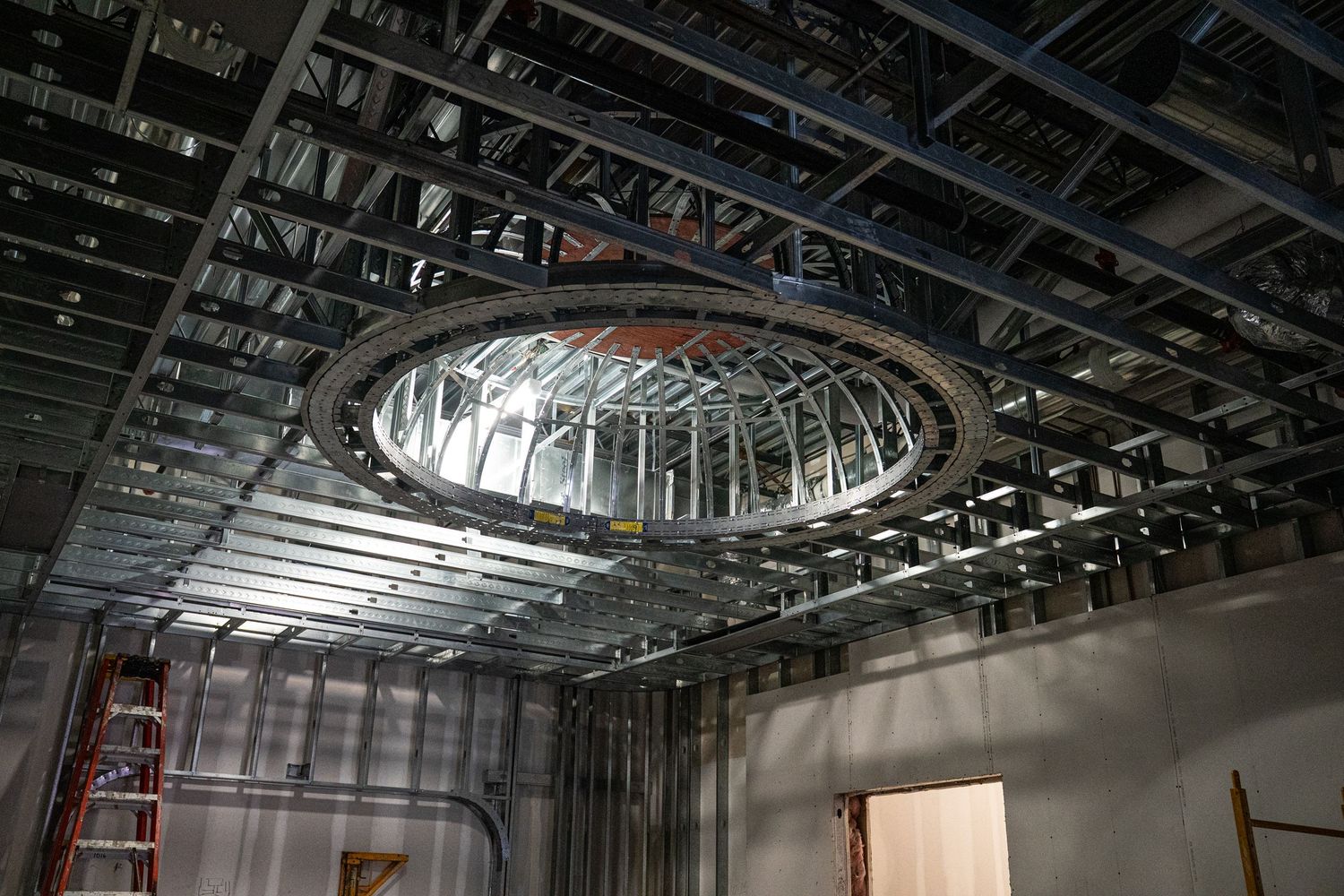 Dramatic circular skylight frame installed in commercial space under construction with exposed metal framing.