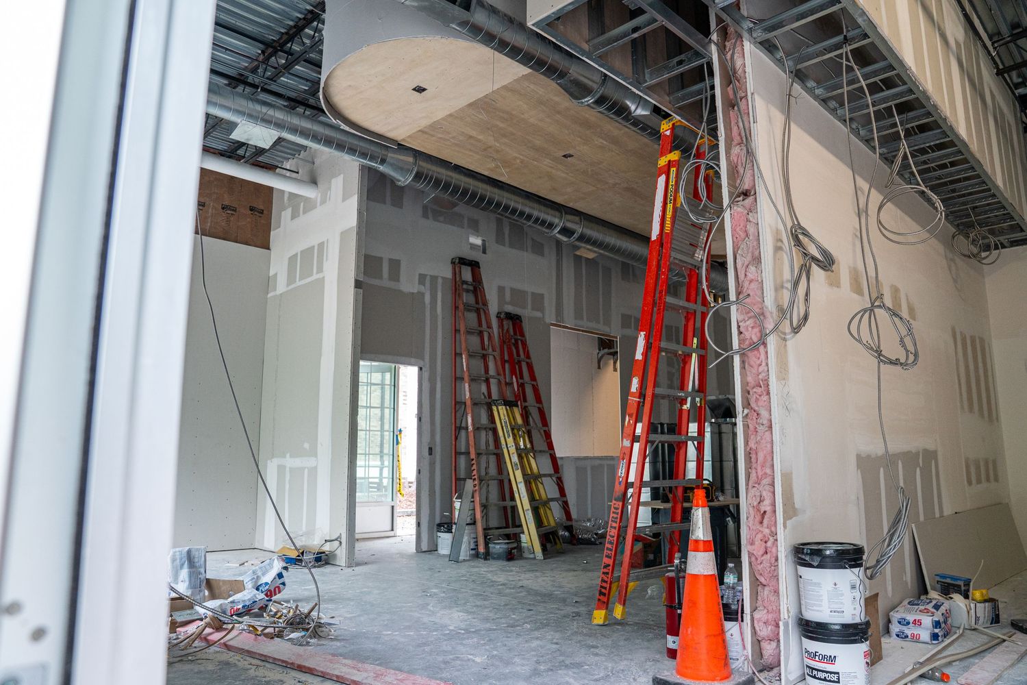 Wide angle view of empty retail space during renovation with visible HVAC and electrical work.