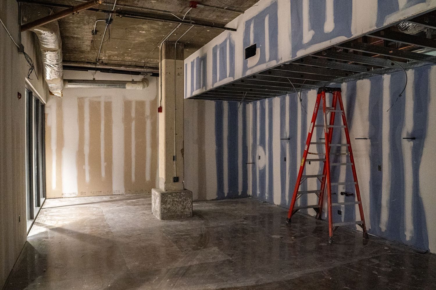 Wide angle view of commercial space under renovation with drywall and exposed ceiling.