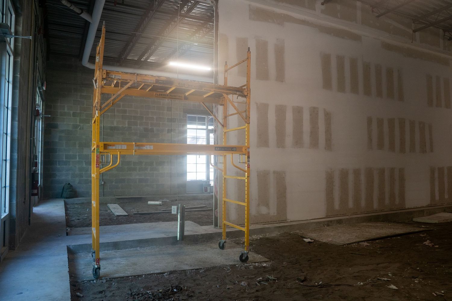 Yellow scaffolding stands against white drywall in unfinished commercial space with exposed ceiling.