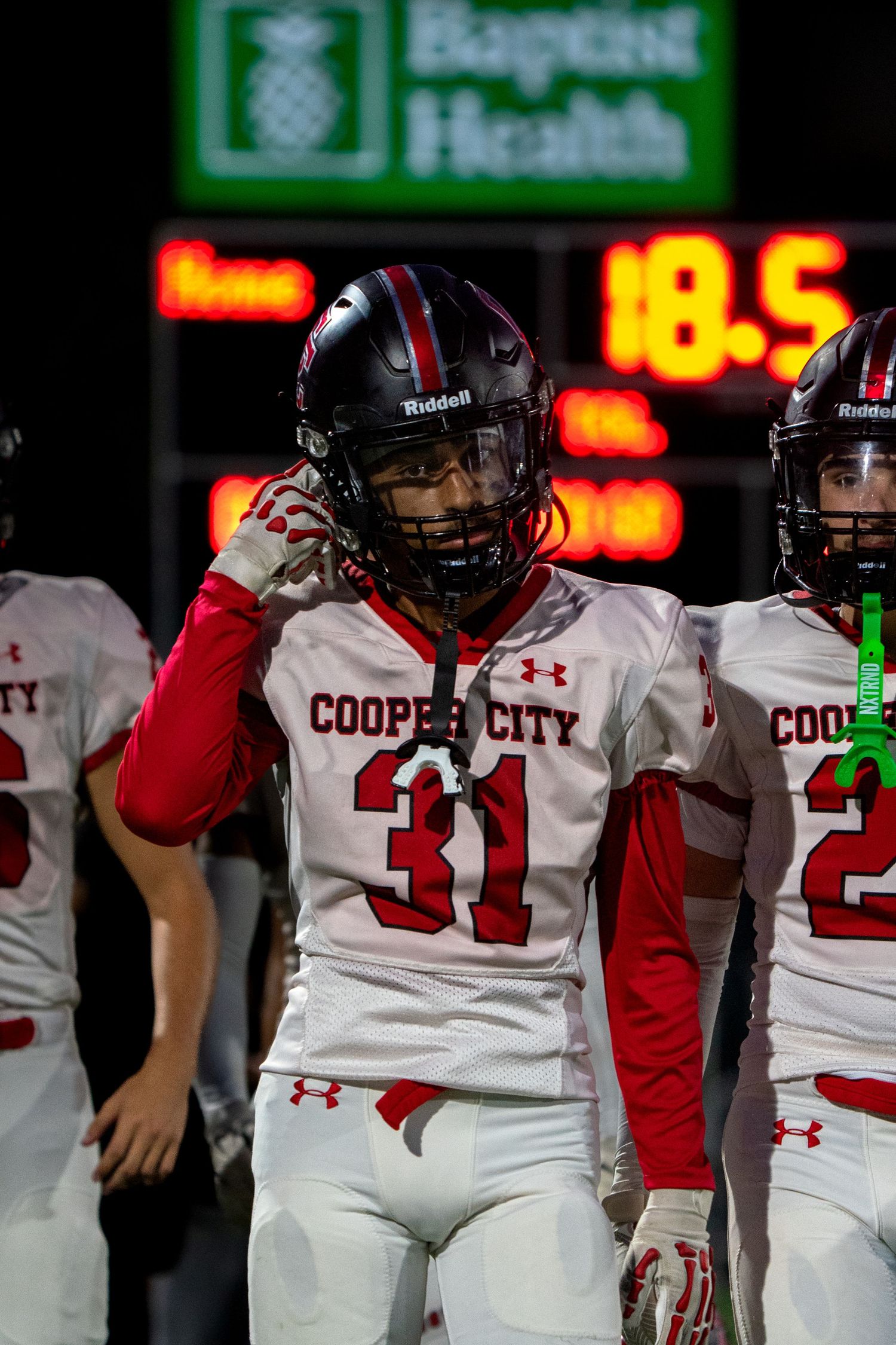 Football players in Cooper City uniforms lined up on the sideline during a night game.