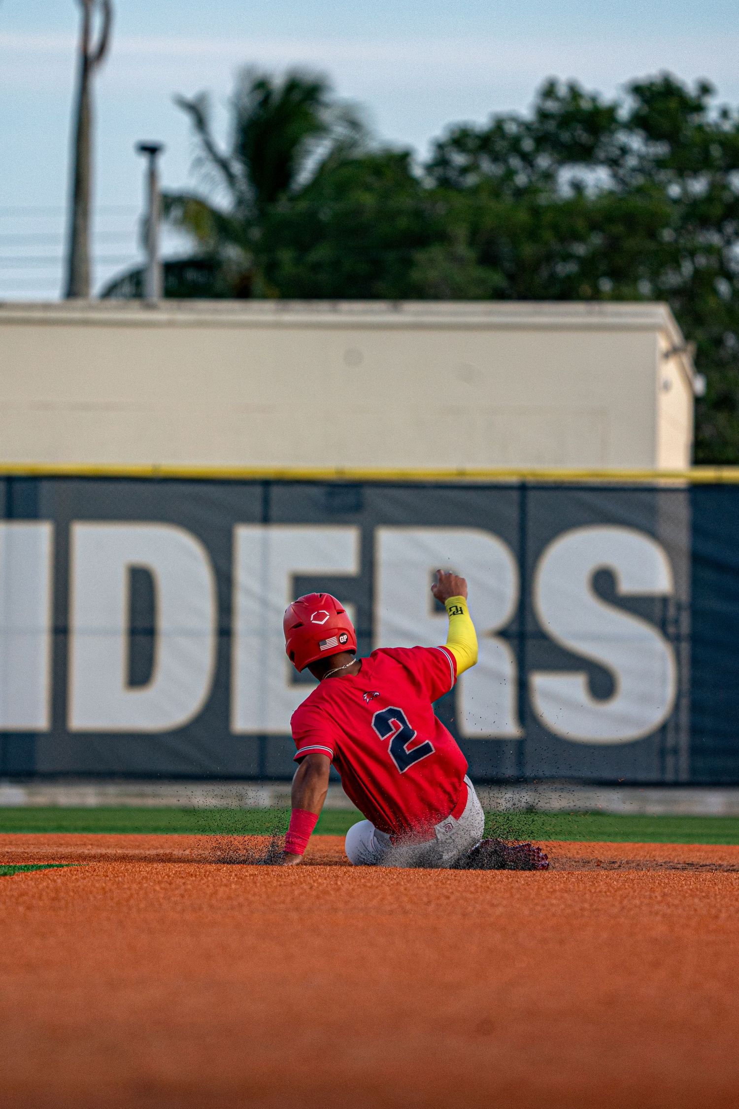 Baseball player in red uniform slides into base creating a cloud of dirt on the infield.