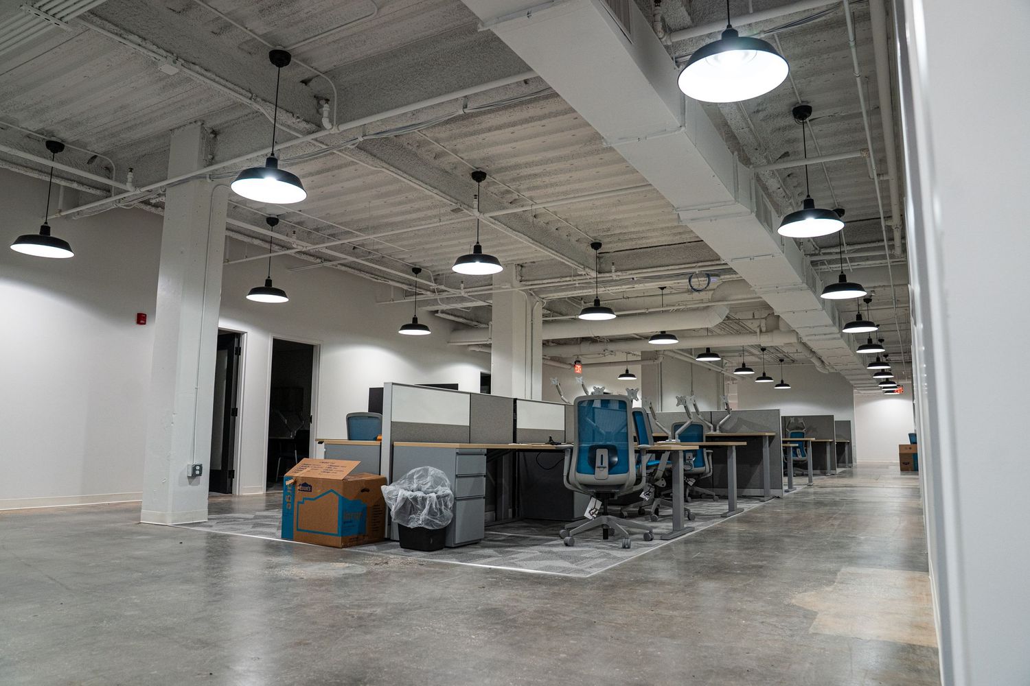 Industrial space with exposed ceiling, pendant lights, and white support columns.