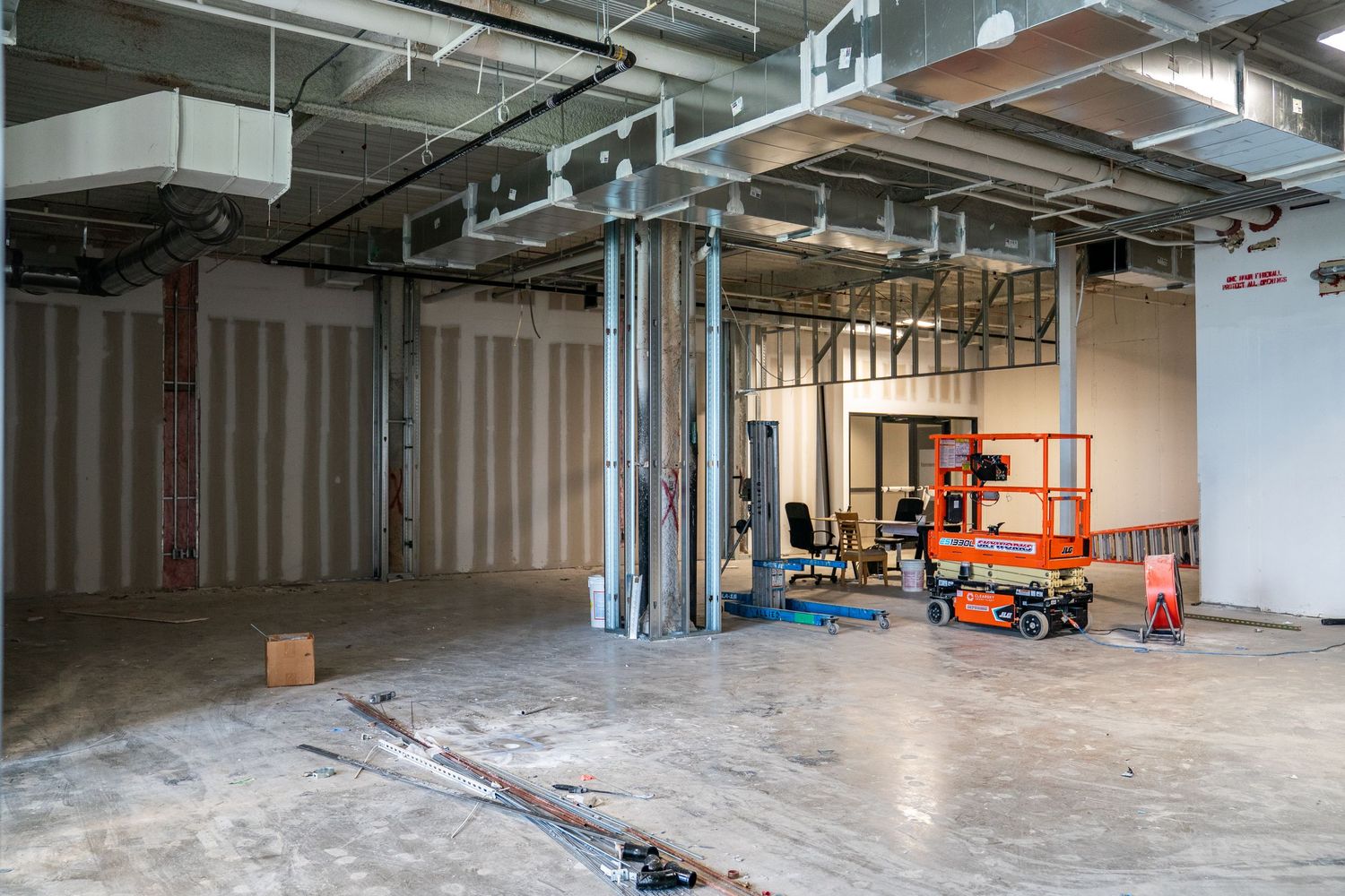 Industrial space undergoing renovation with exposed ceiling systems and construction equipment.