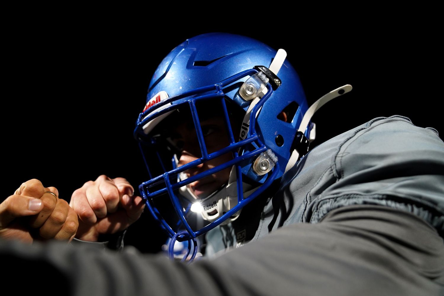 Close-up view of blue football helmets worn by players on the sideline.