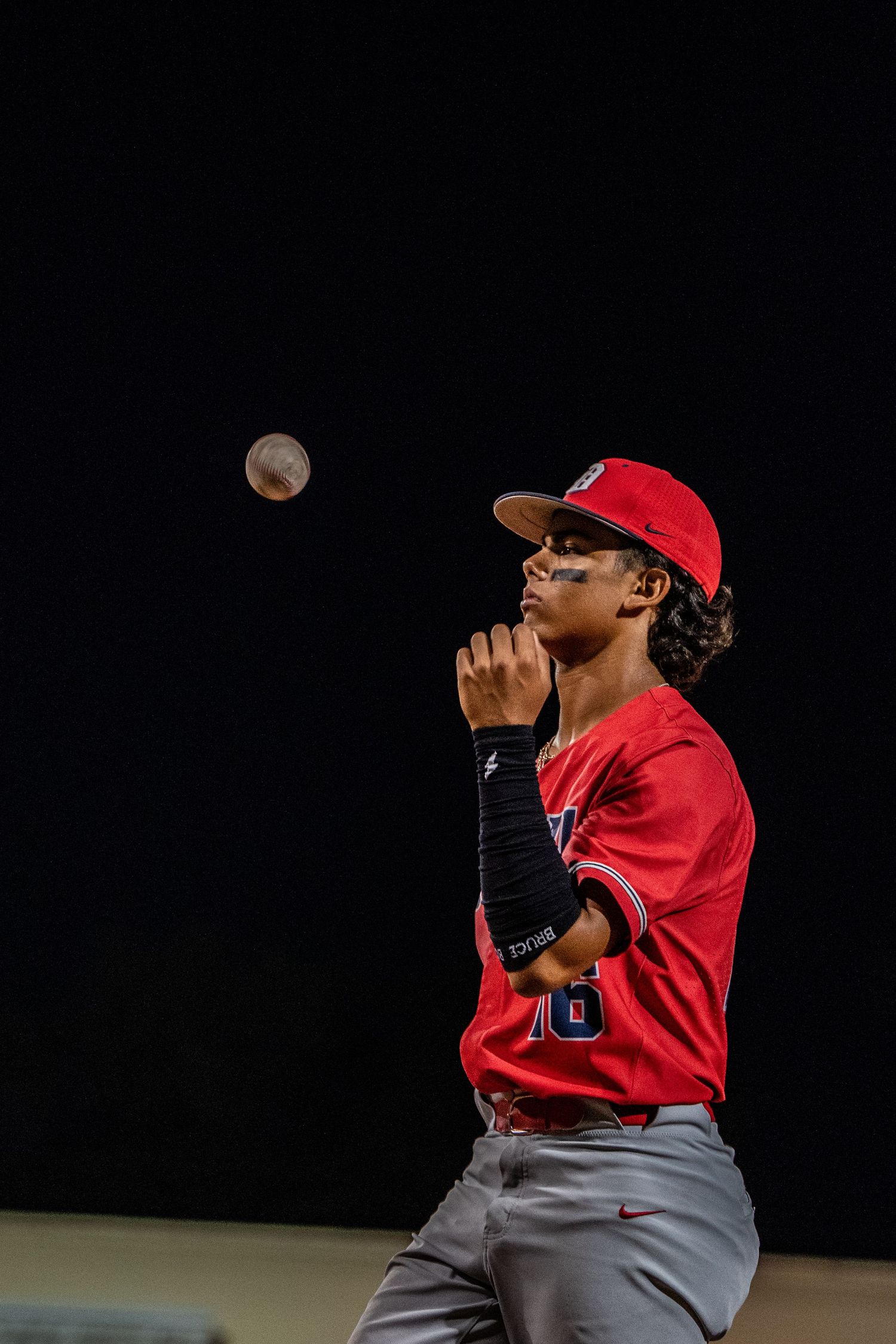 Baseball pitcher in red uniform throwing a pitch during night game.