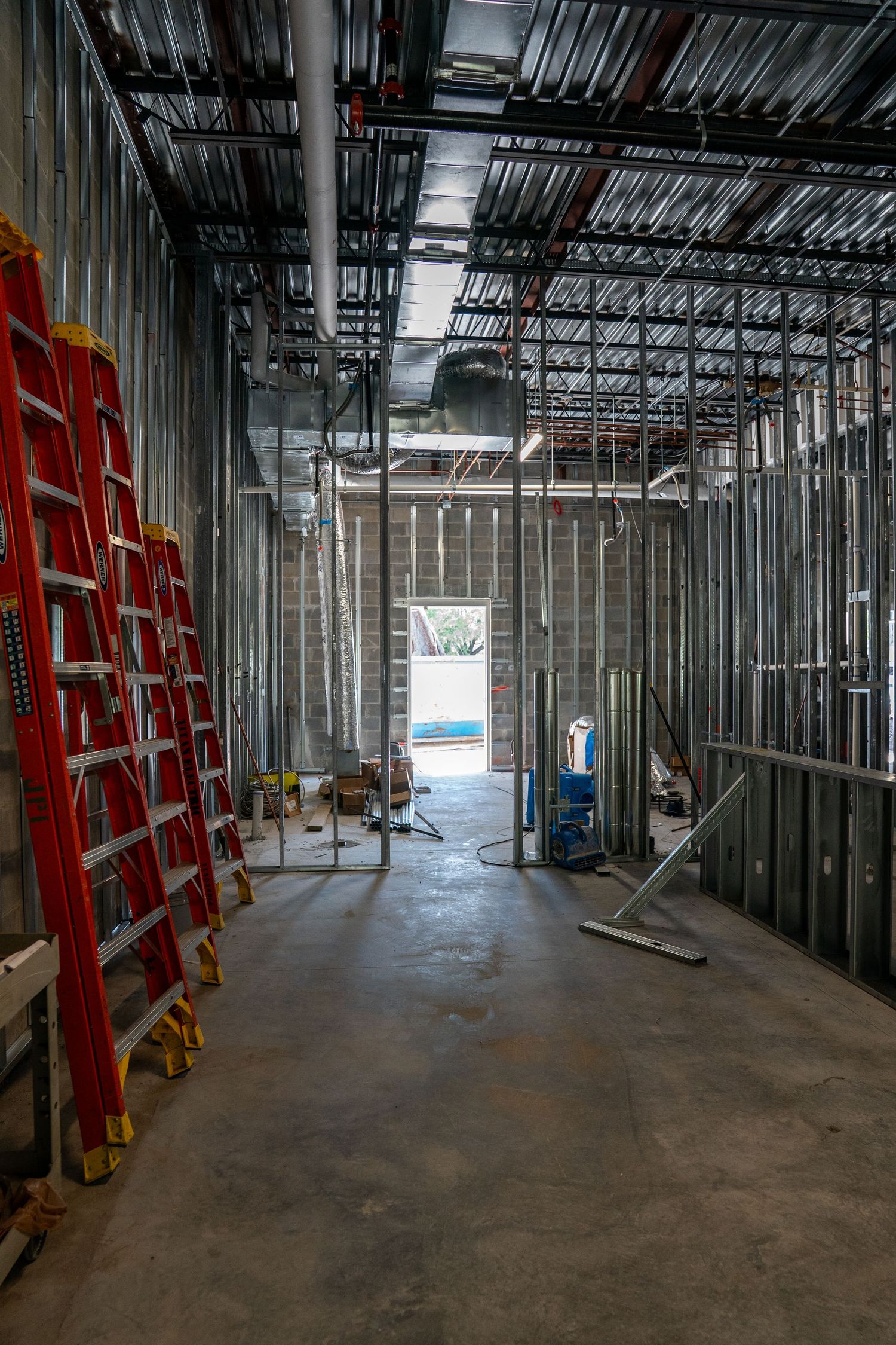 Construction site interior showing metal framing and red ladders along unfinished walls.