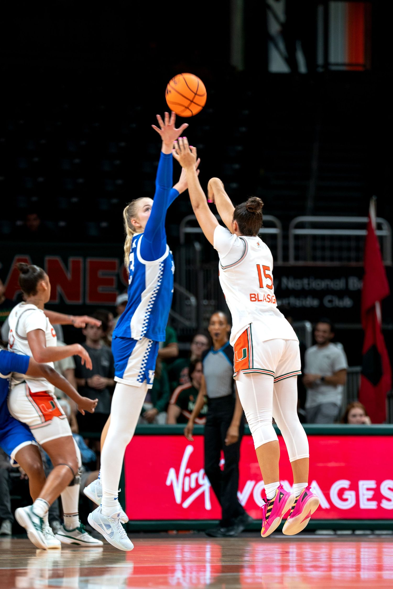 Basketball players jump and reach for the ball during an intense game moment.