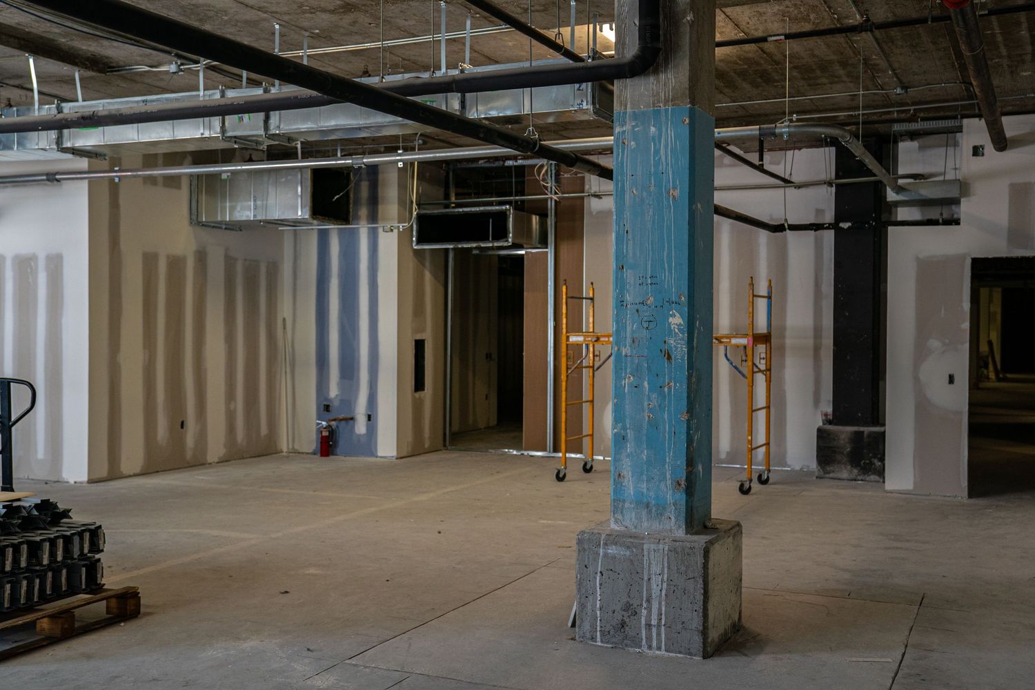 Industrial warehouse space with exposed ductwork and support columns during renovation.