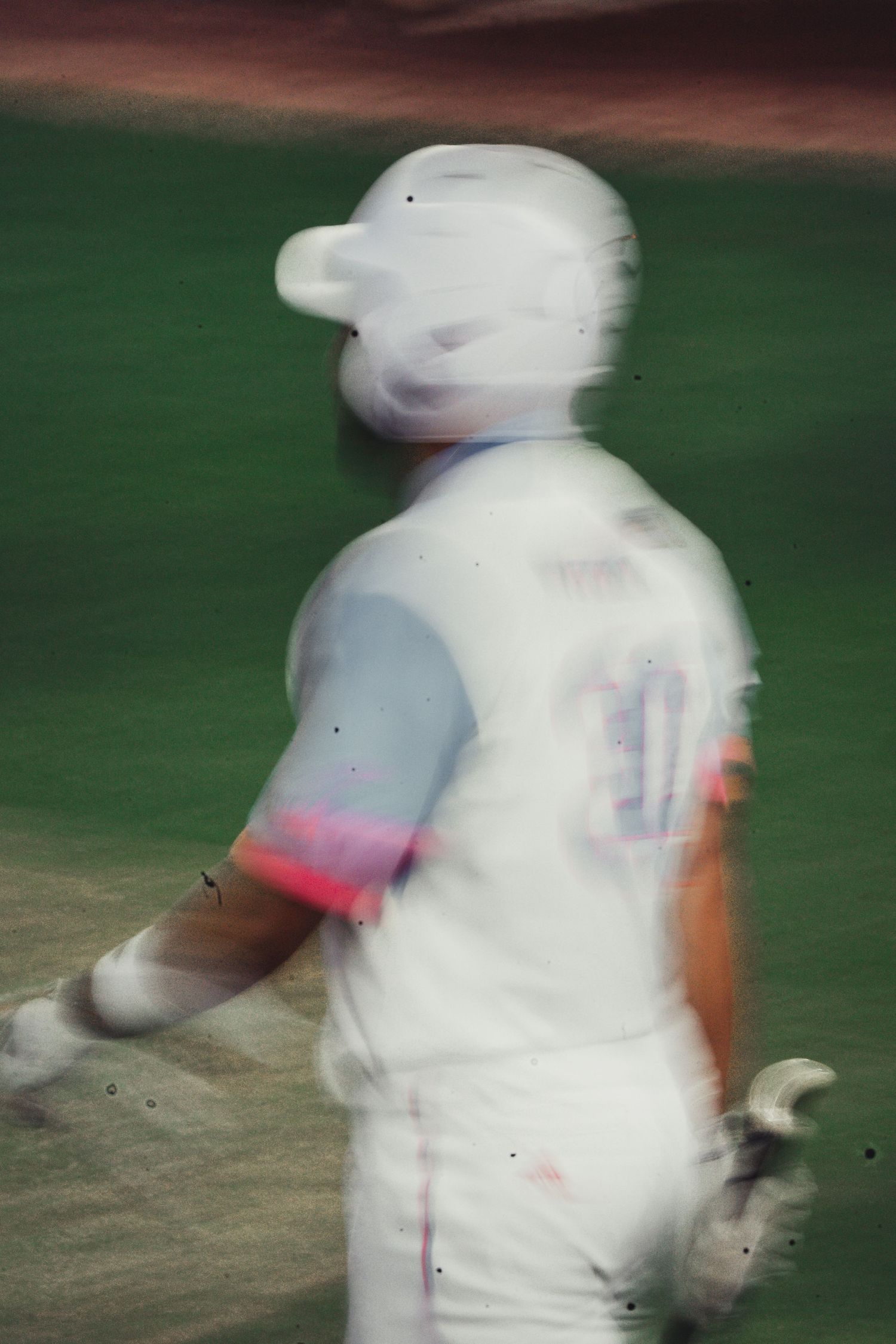 Blurred motion shot of a baseball player in white uniform with colorful sleeve details during a game.