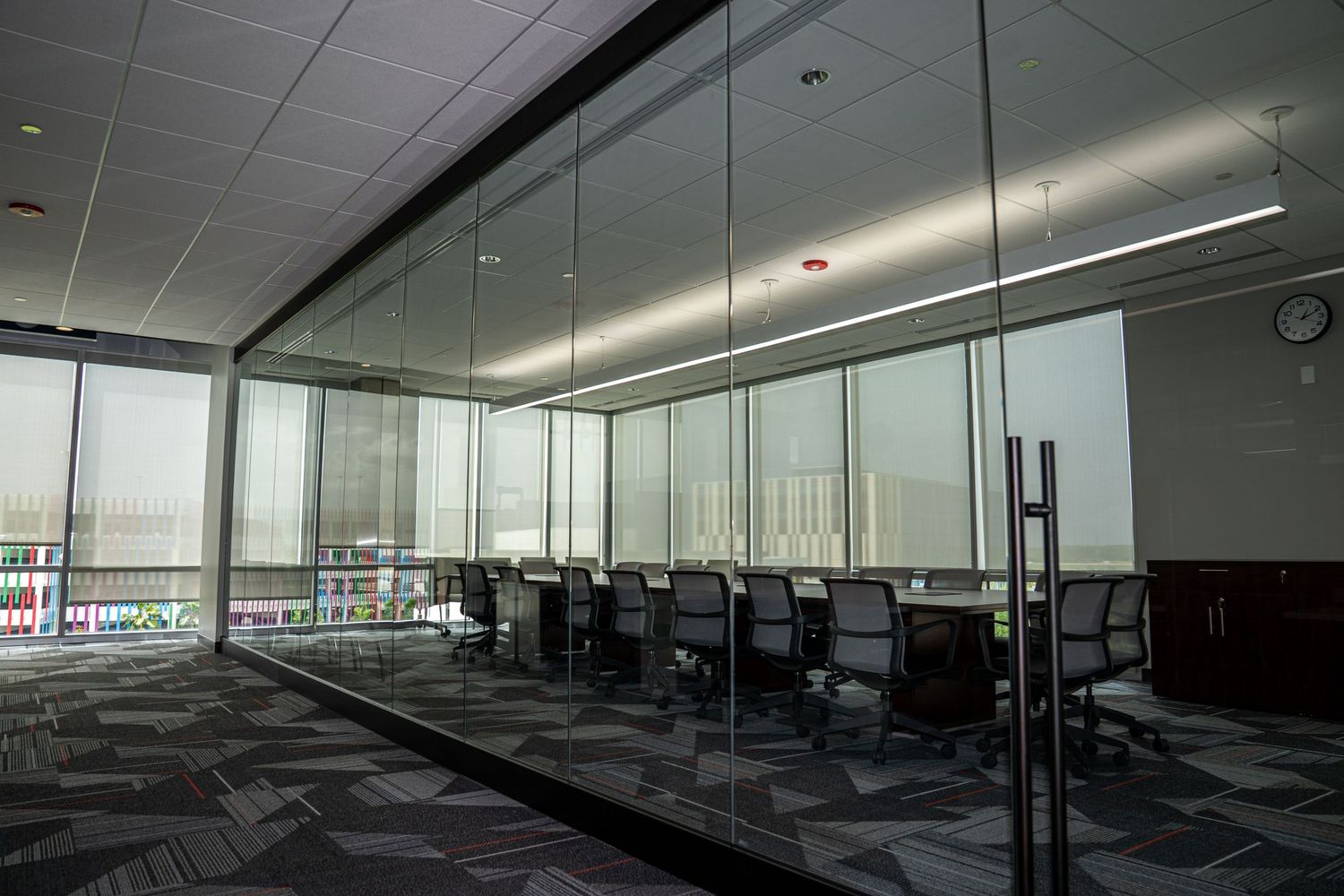 Professional meeting room with glass partitions and modern workstations on patterned carpet.
