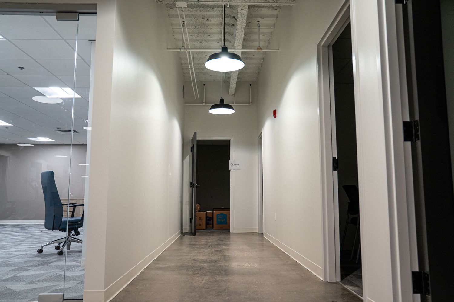 Long white hallway with pendant lighting and doors along the walls under construction.