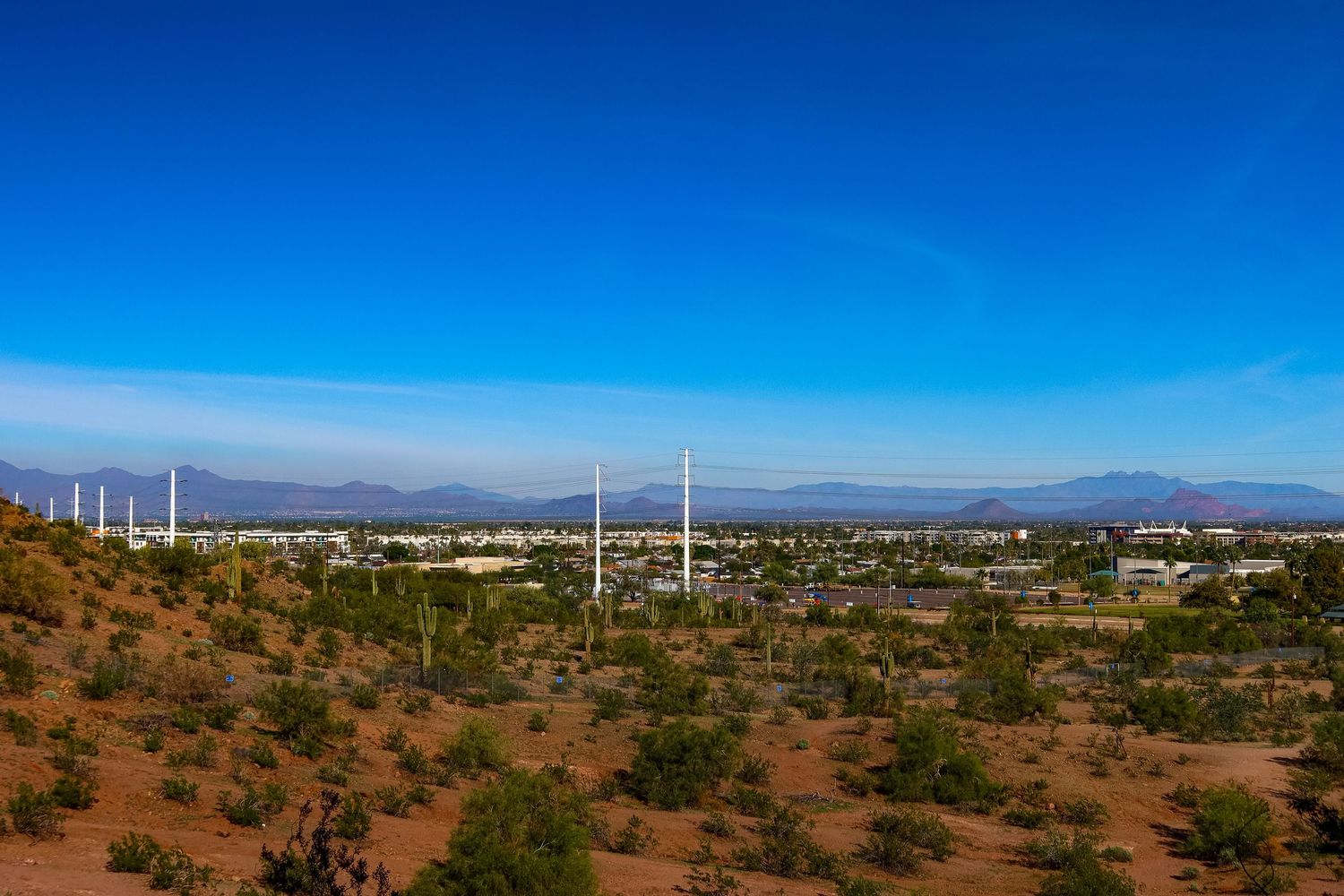 Desert valley with power lines stretching across arid terrain and mountains in the distance.