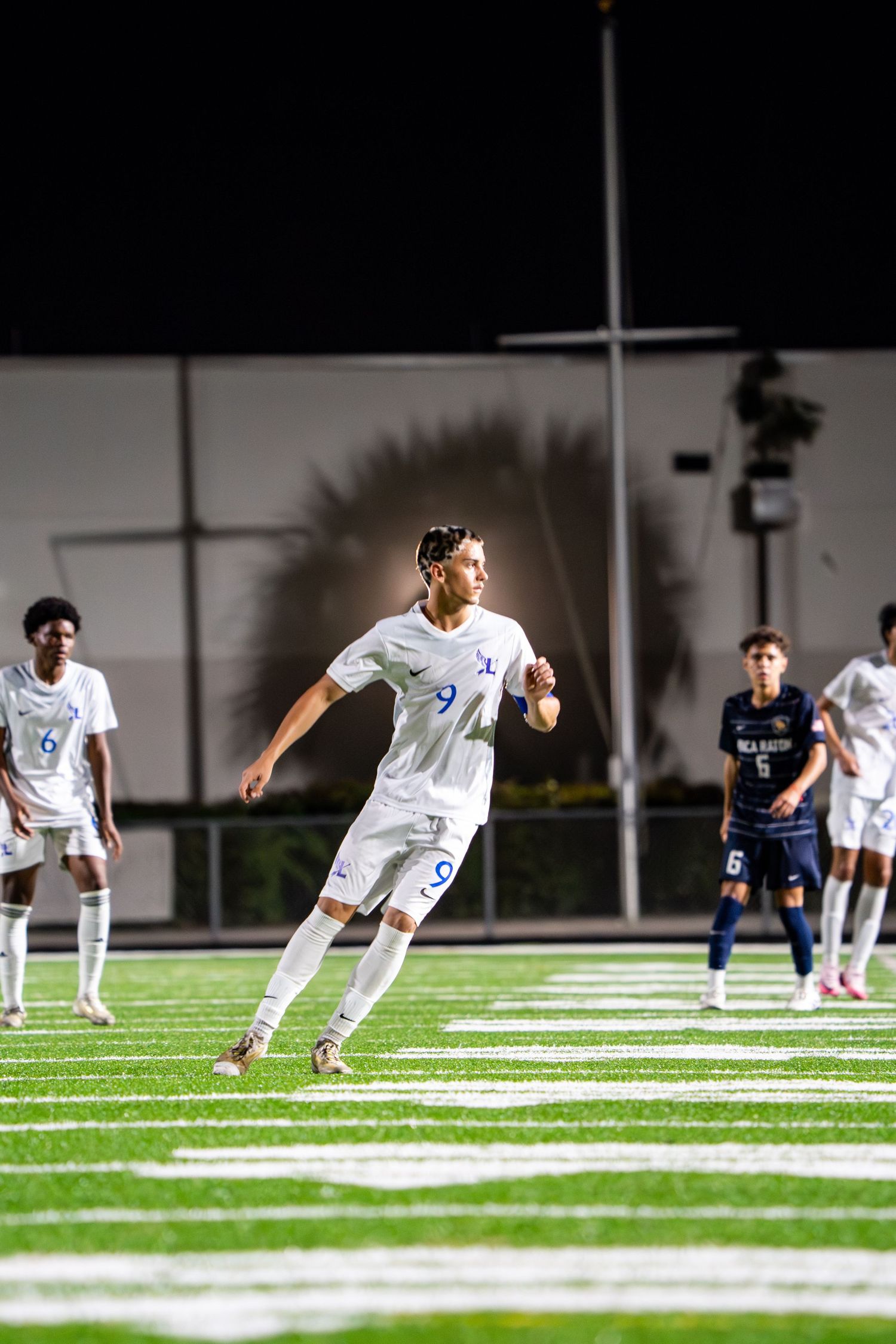 Soccer players in white uniforms stretching on a floodlit field at night.