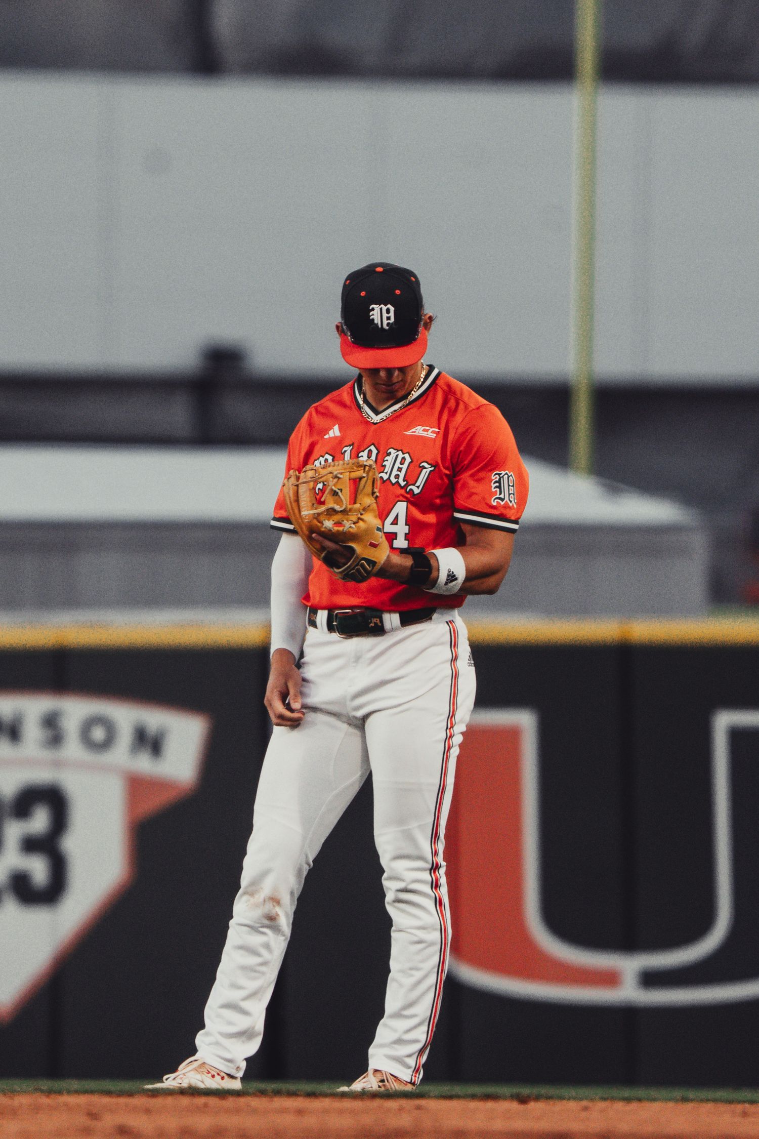 University of Miami baseball player #4 in red uniform stands on field holding glove during college game.