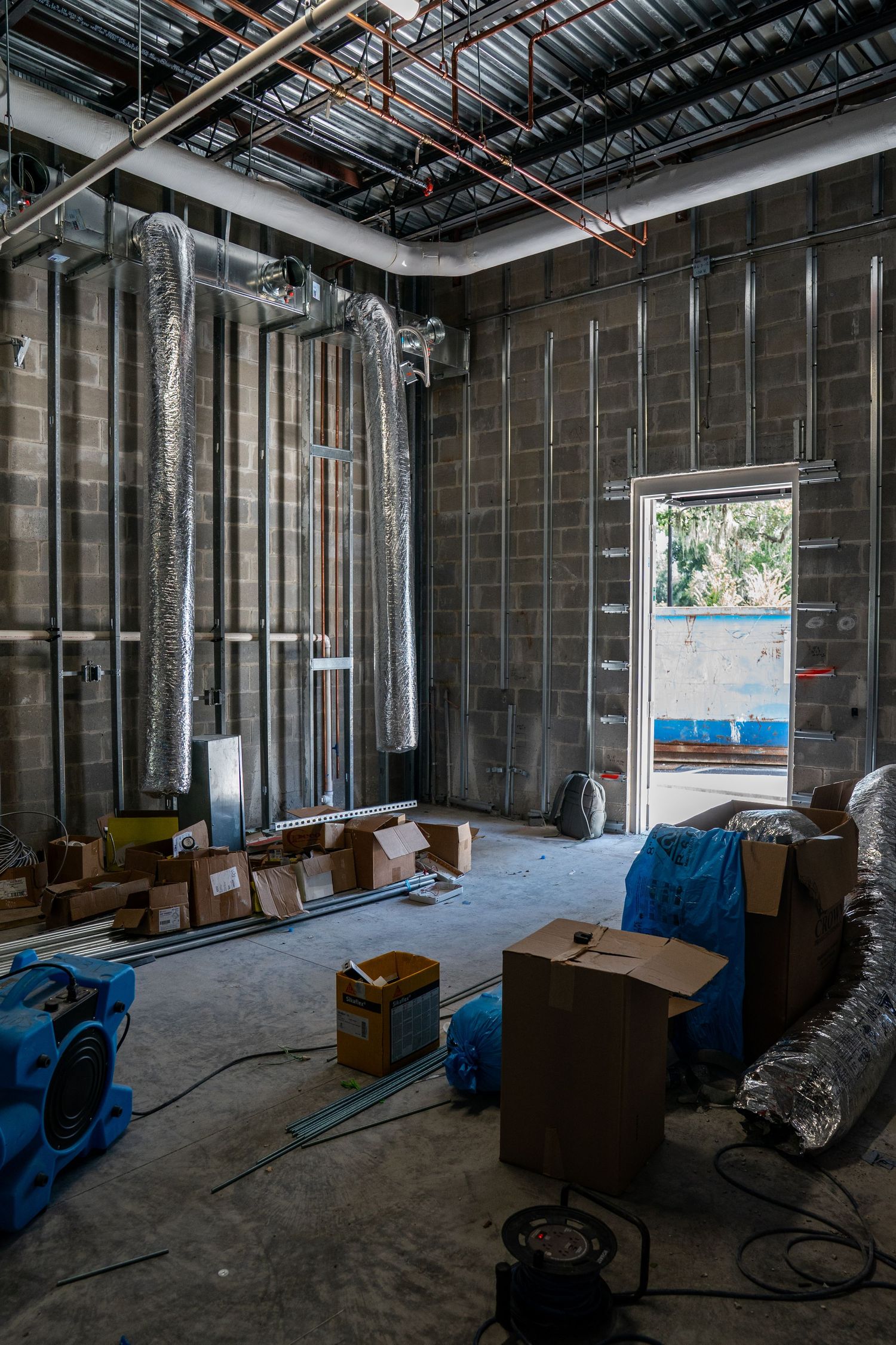 Commercial construction site with metal framing, exposed ductwork, and blue equipment.
