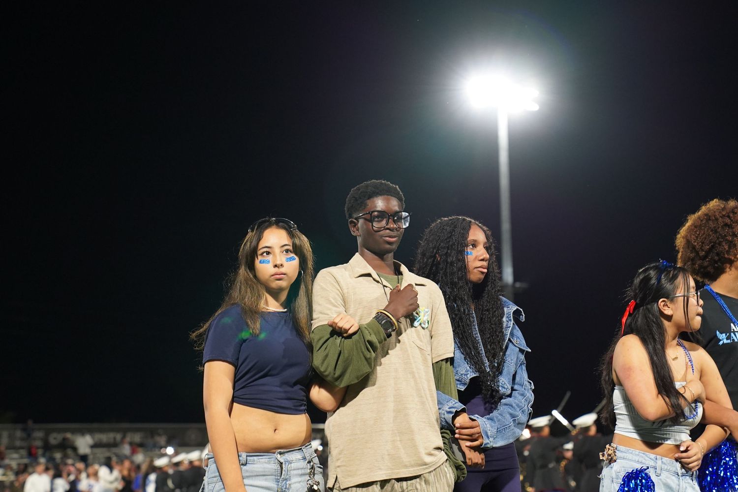 Students line up on a dark field lit by stadium lights during an evening event.