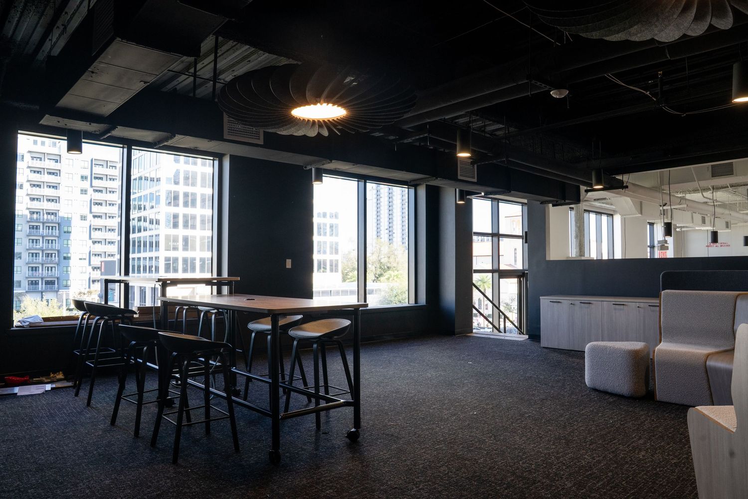 Modern office interior with exposed ceiling, large windows, and open floor plan layout providing natural light.