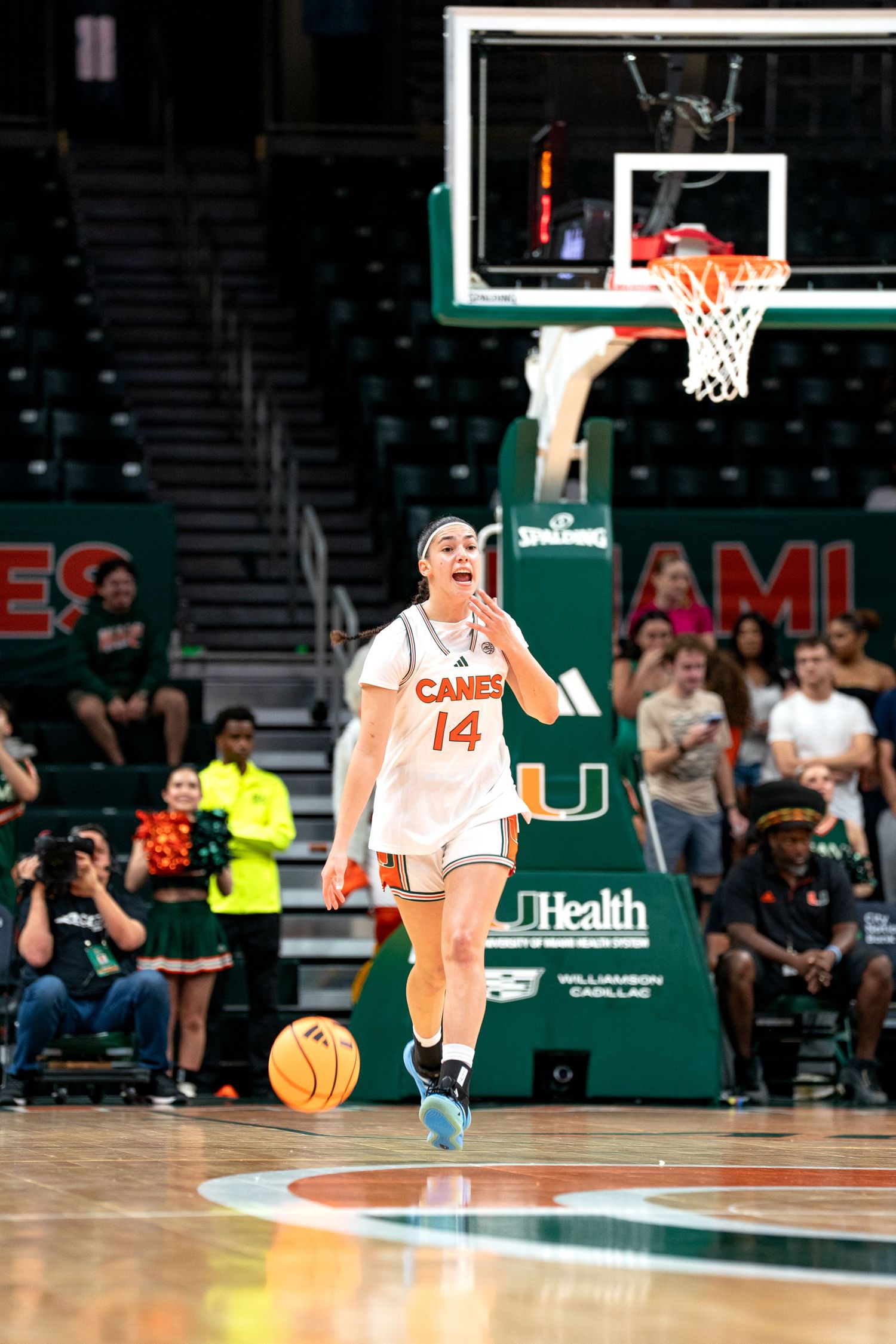 Player in white Miami uniform dribbles basketball near court sideline.