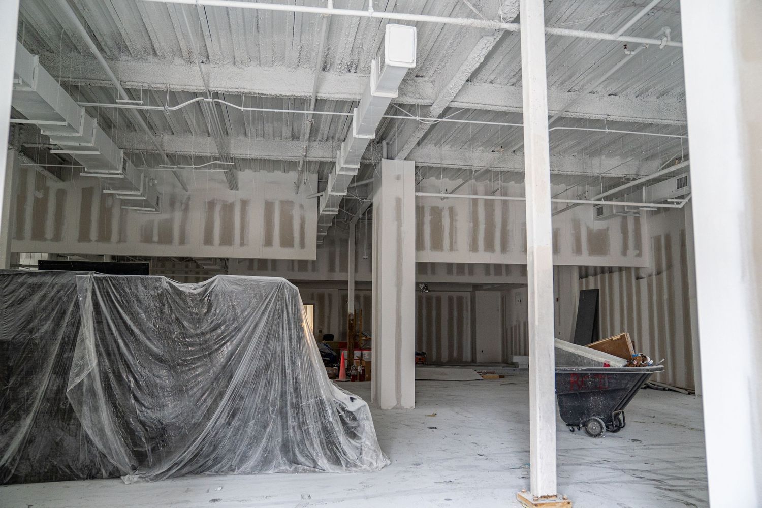 Wide open industrial space with white support columns and plastic-covered areas.