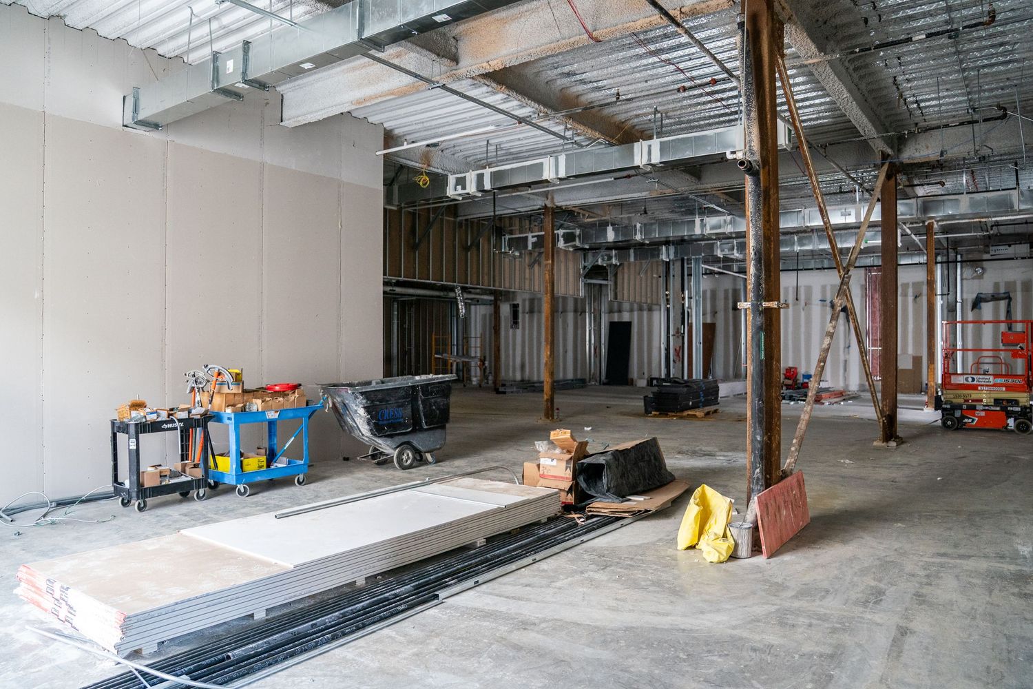 Construction site interior showing metal framing, support poles, and building materials in an open space.