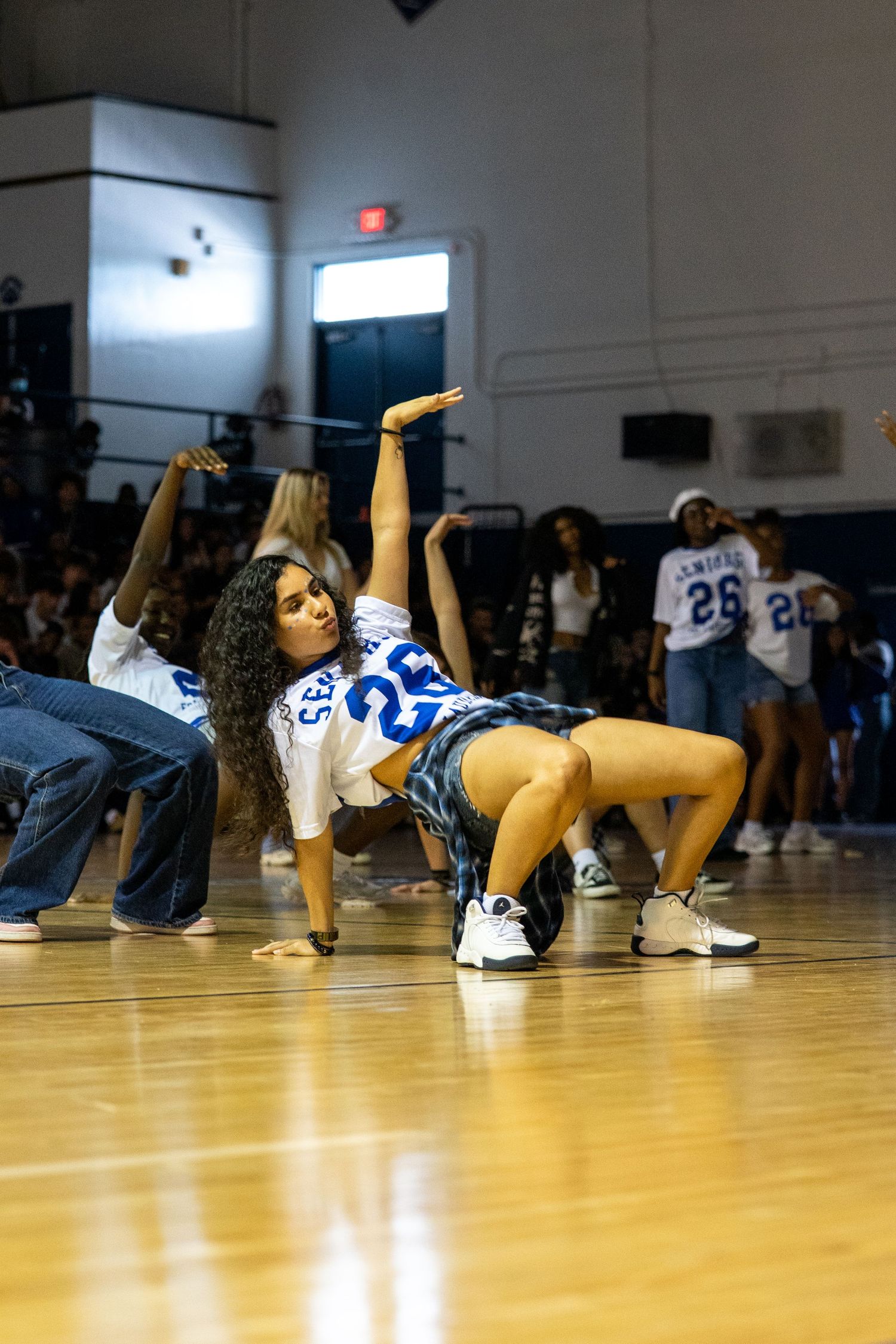 Students perform energetic dance routines in jerseys on a gymnasium floor during a school pep rally event.