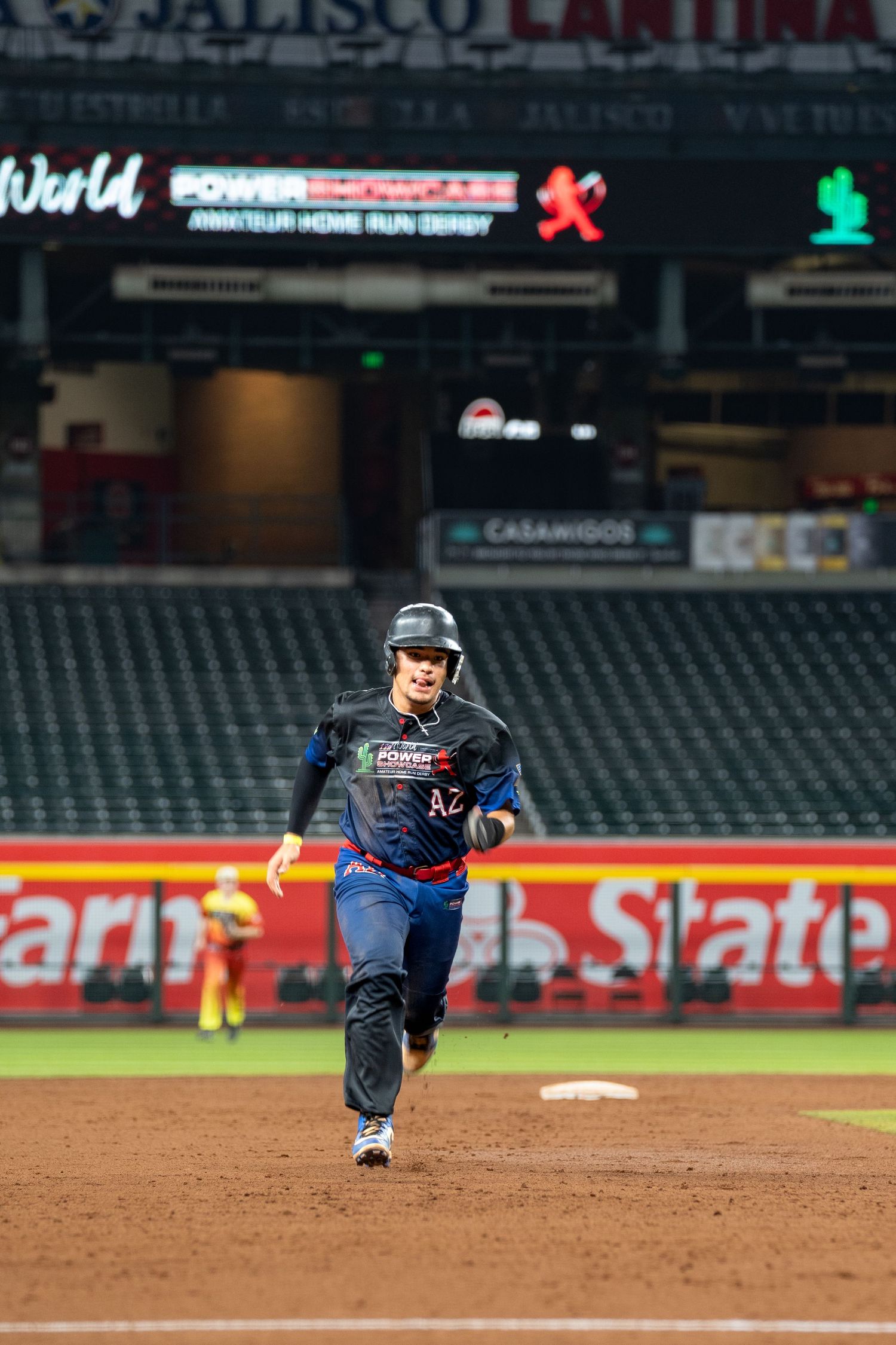 Baseball player in dark uniform slides across the infield dirt during a game at night.