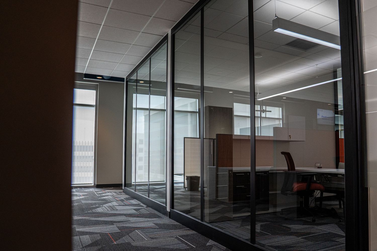 Modern office space with glass walls, exposed ceiling, and natural lighting shows an empty interior under construction.