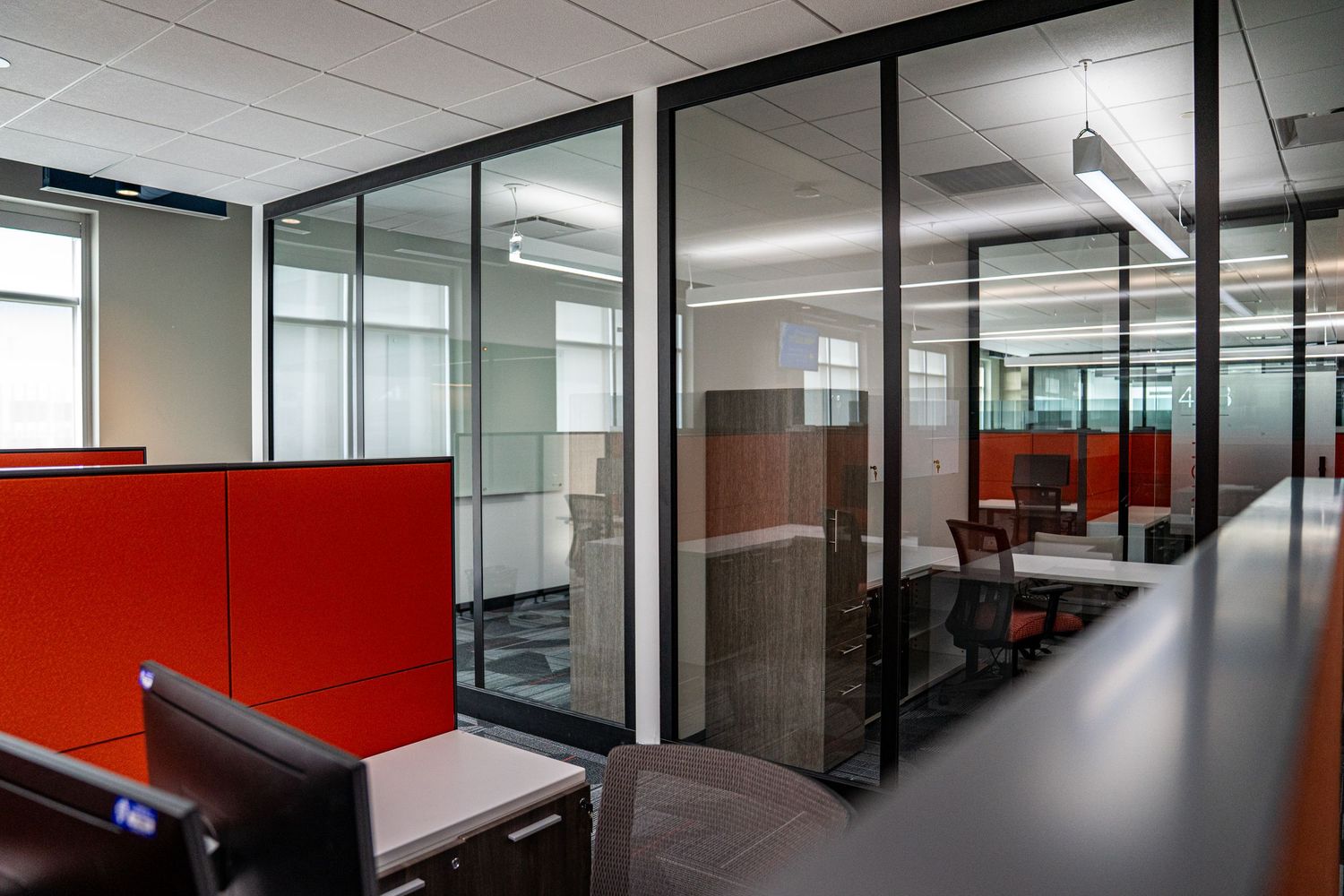 Contemporary office interior featuring red dividers and glass-enclosed workspaces with modern furnishings.