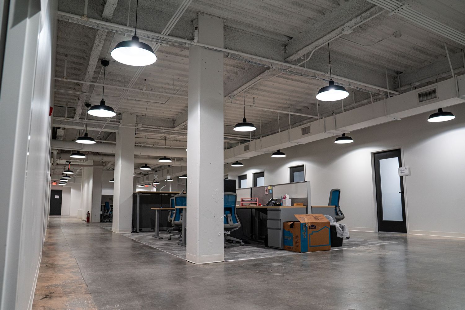 Wide angle view of vacant commercial interior with exposed ductwork and lighting.