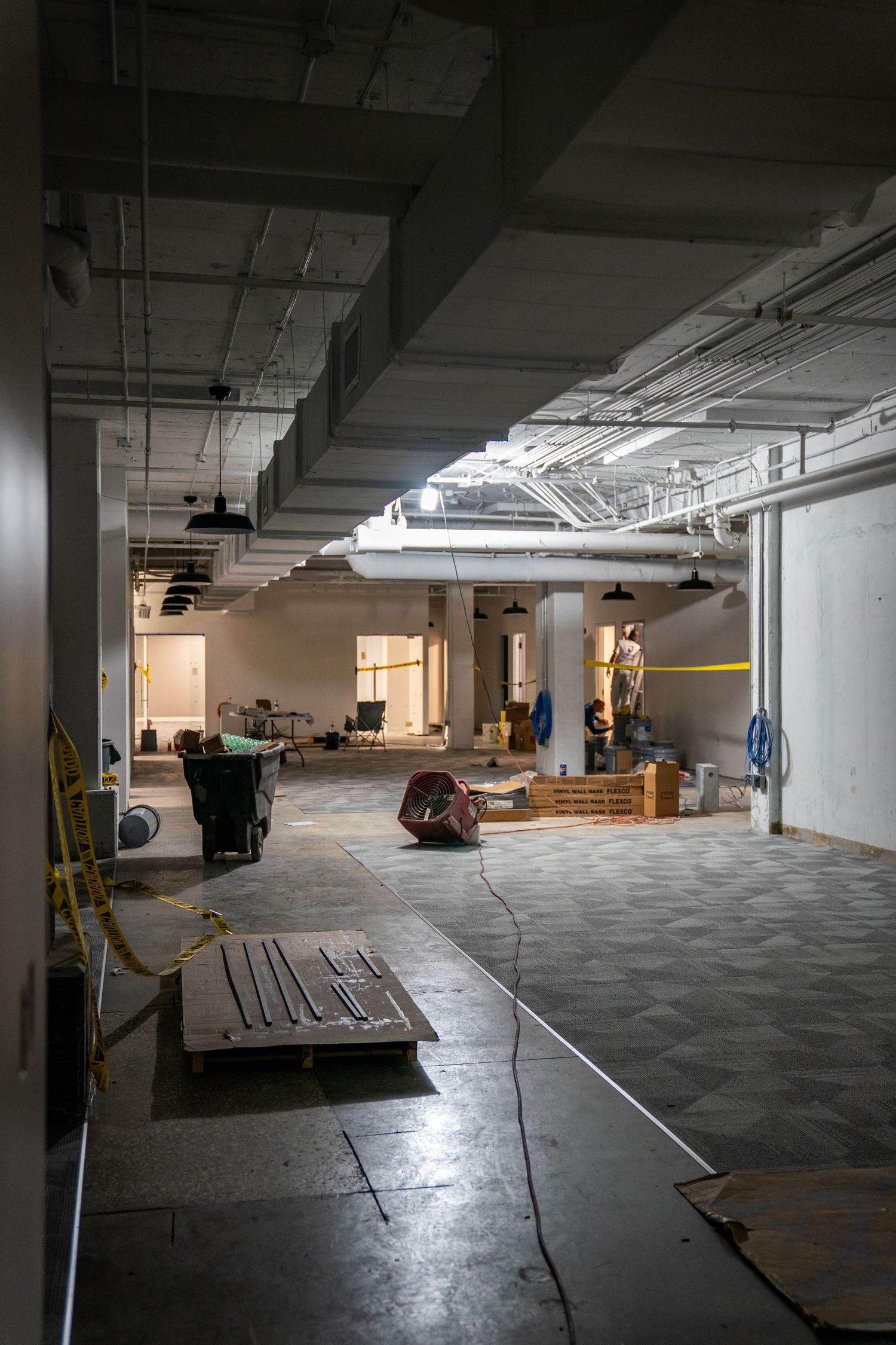 Large empty commercial space under construction with concrete floors and exposed ceiling infrastructure.