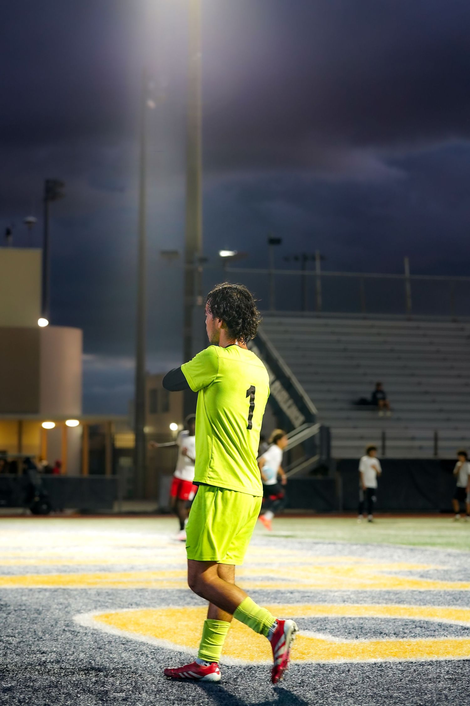 Soccer goalkeeper in neon yellow uniform positions themselves during night game.
