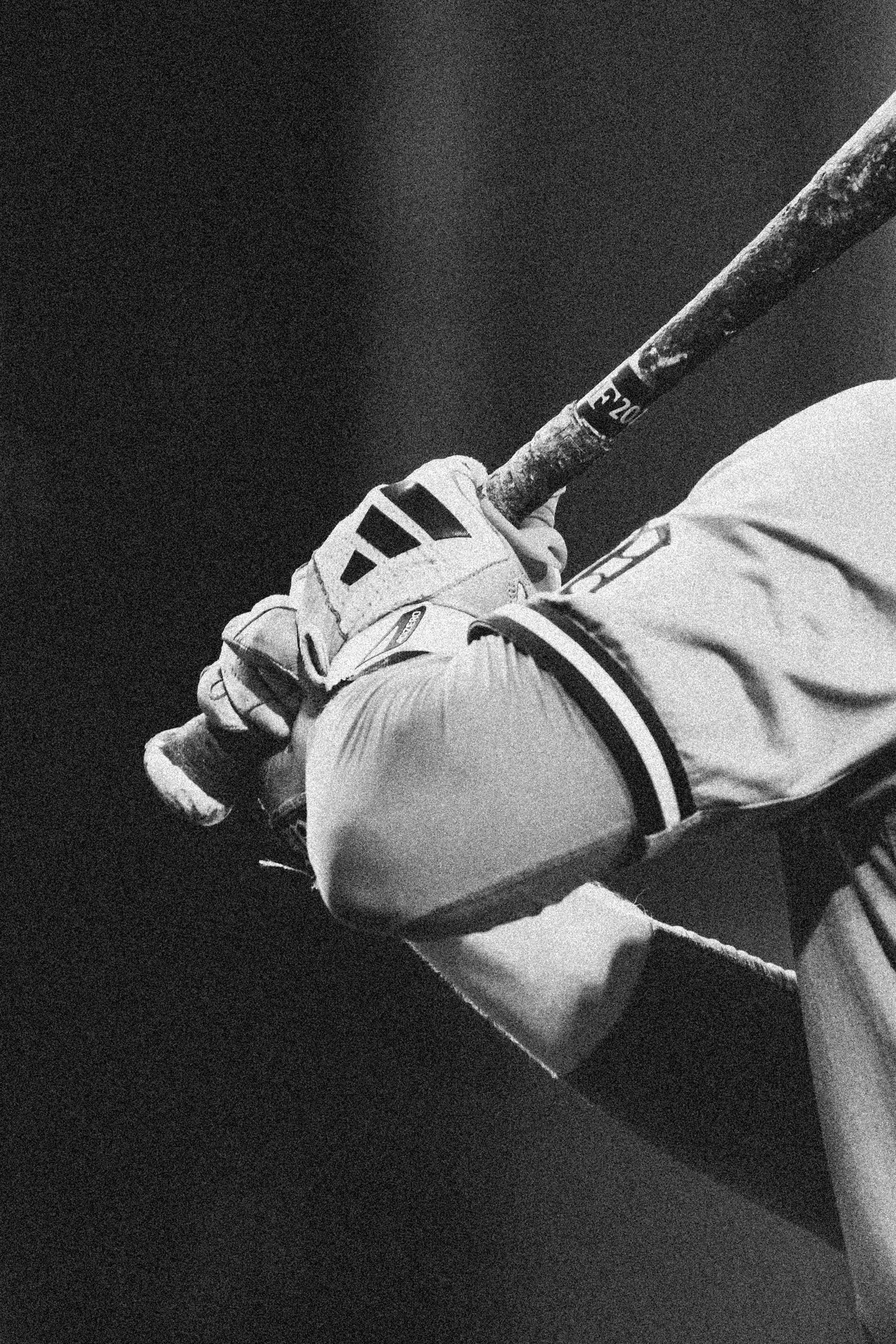 A black and white close-up of a baseball batter gripping a bat wearing batting gloves.