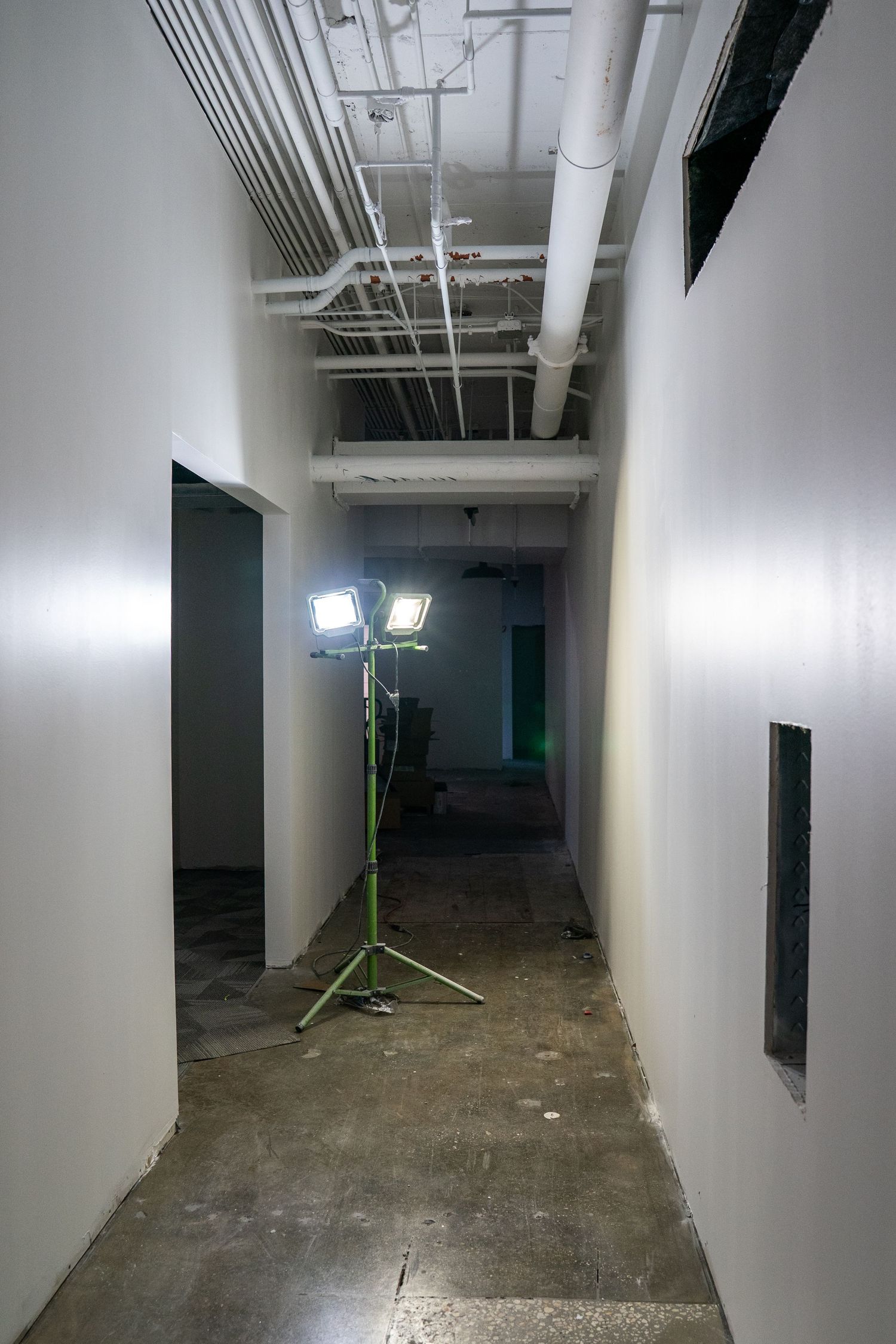 Construction site hallway with bright work lights and exposed utilities overhead.
