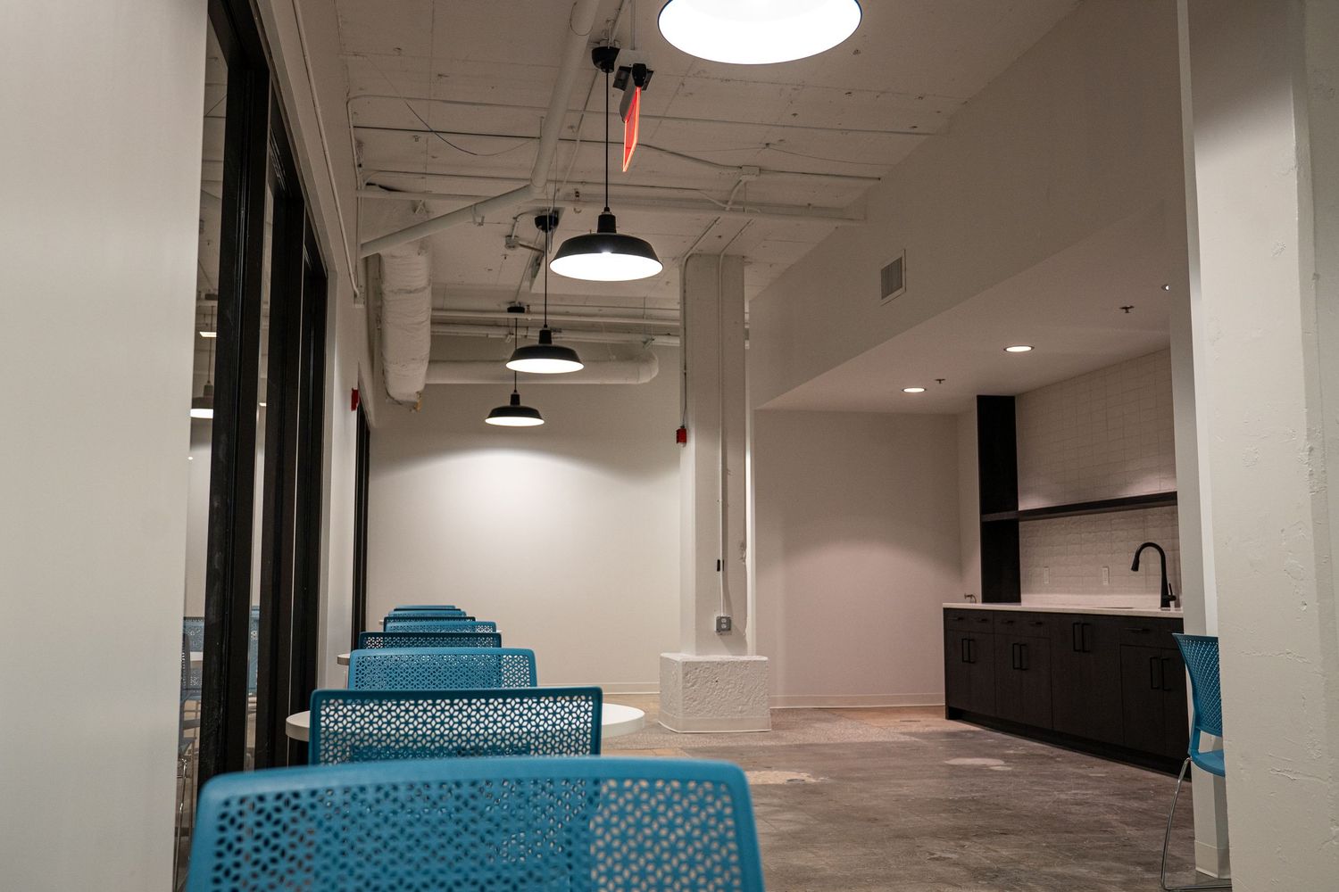 Modern break room with blue chairs and kitchenette under industrial ceiling.