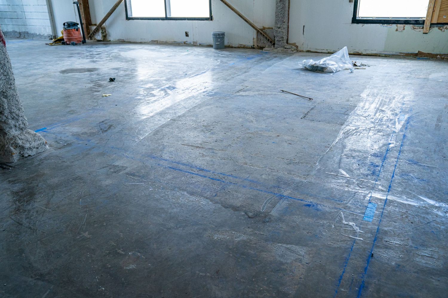 Empty commercial space with windows and blue markings on concrete floor during construction.