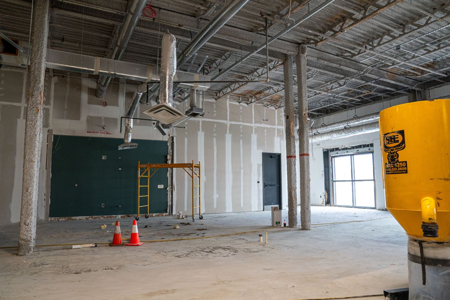 Interior construction site showing unfinished commercial space with exposed ceiling, green chalkboard, and orange wall.