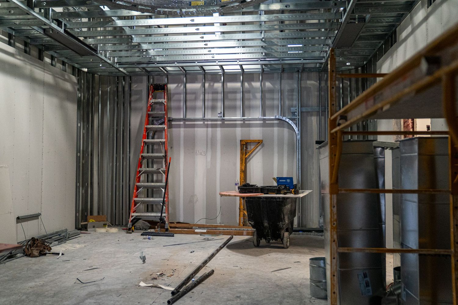 Unfinished commercial space with metal studs, red ladder, and construction materials visible.