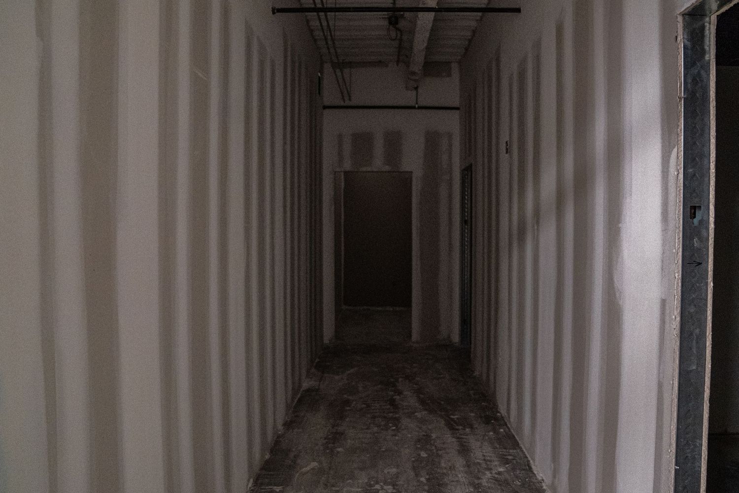 Long empty corridor with white walls and exposed ceiling ducts under construction.