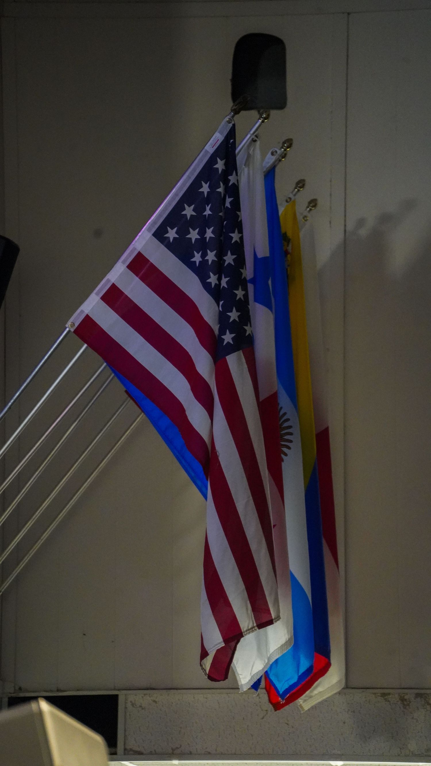 American flag displayed alongside other national flags against white wall.