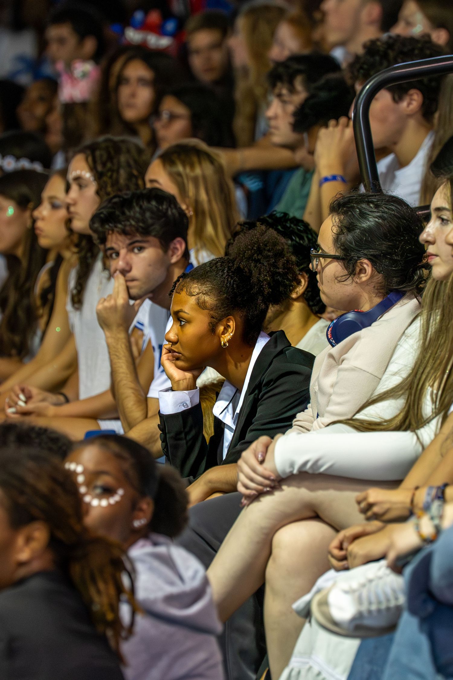 Diverse group of young students sitting attentively in bleachers during a school assembly or event.
