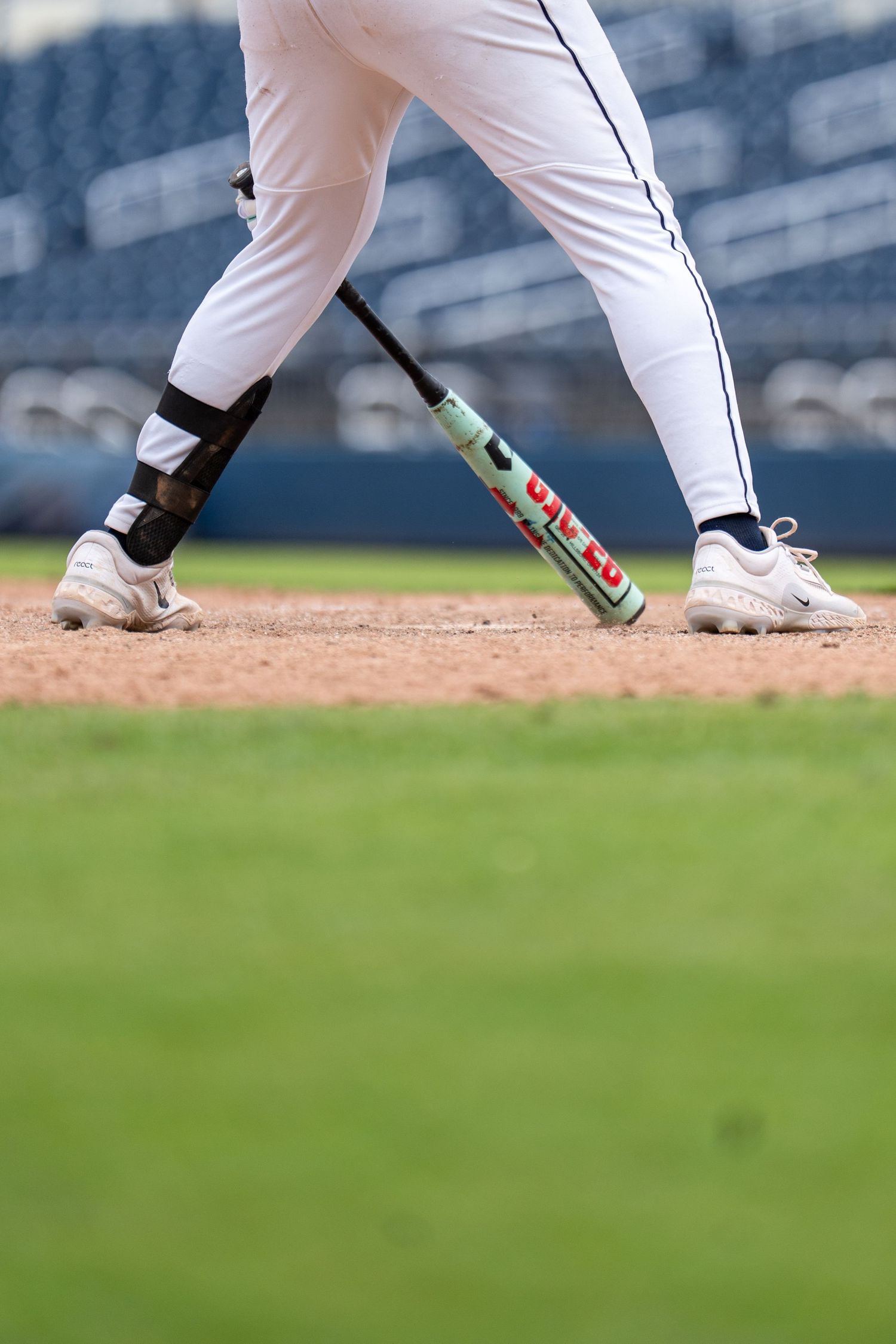 Close-up of baseball player's legs in white uniform holding a bat in batting stance on dirt field.