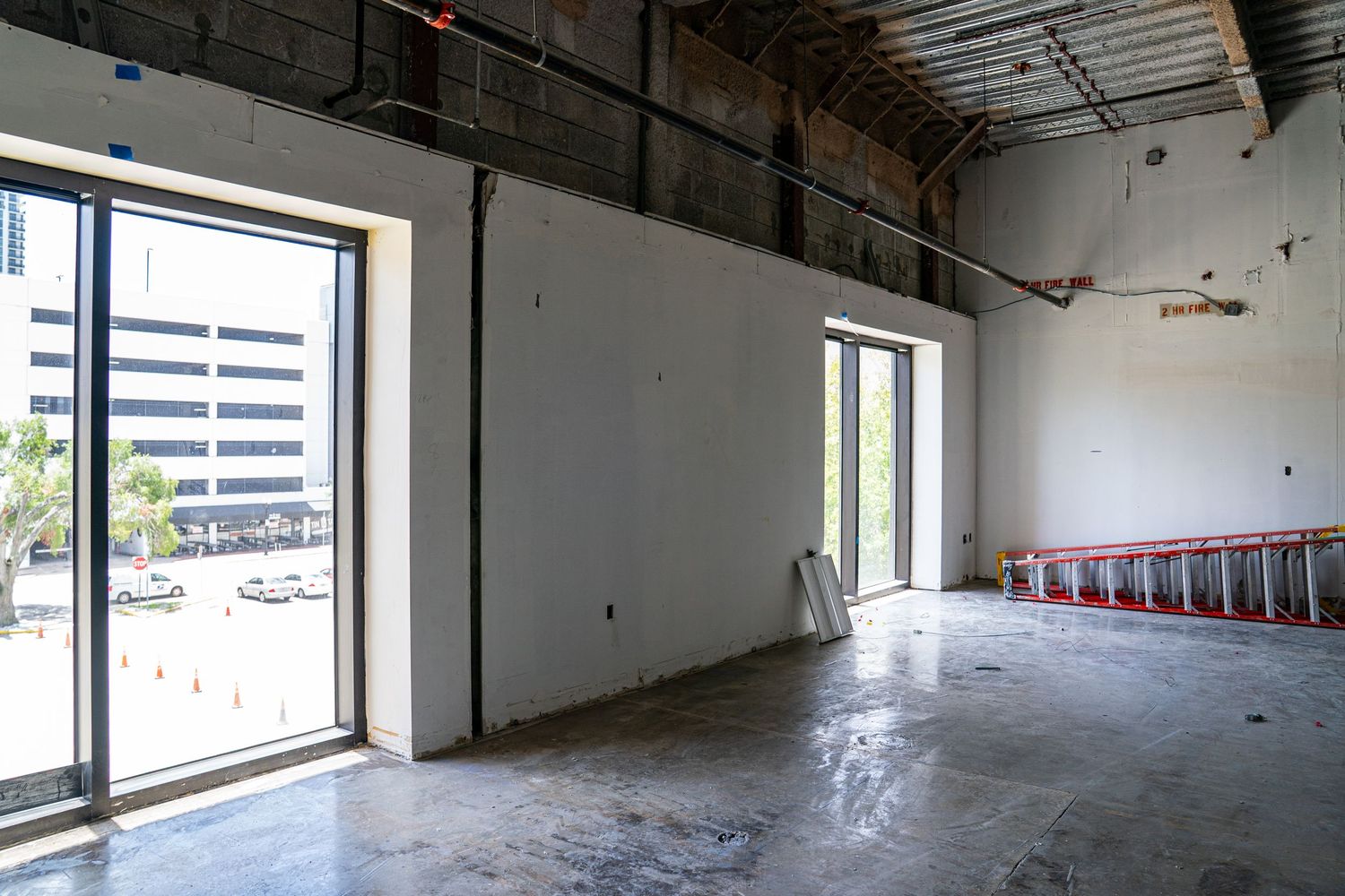 Empty industrial space with large windows providing natural light and exposed mechanical systems.