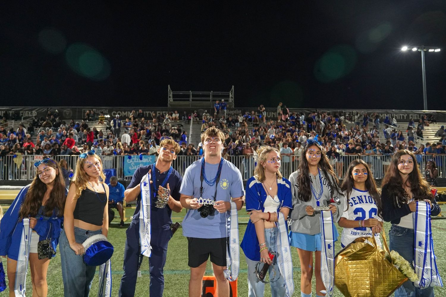 Excited crowd of students cheering in stadium bleachers during a nighttime sporting event.