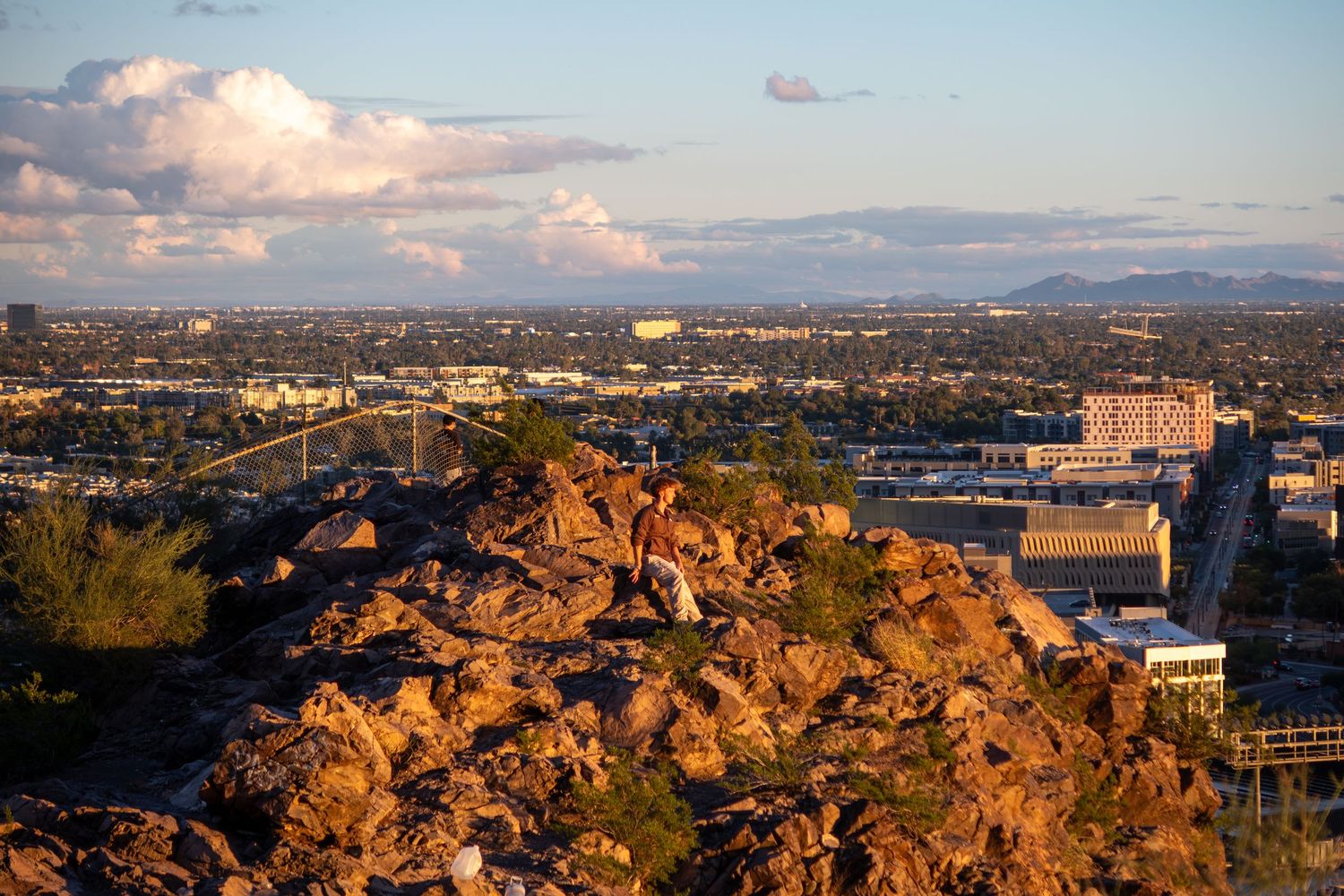 Panoramic cityscape view at sunset with golden light illuminating rocky outcrops and buildings.