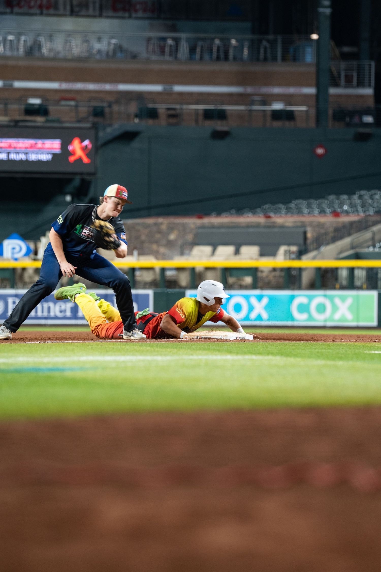 Baseball players in action during a game with one sliding into base while another reaches to make a play at the field.
