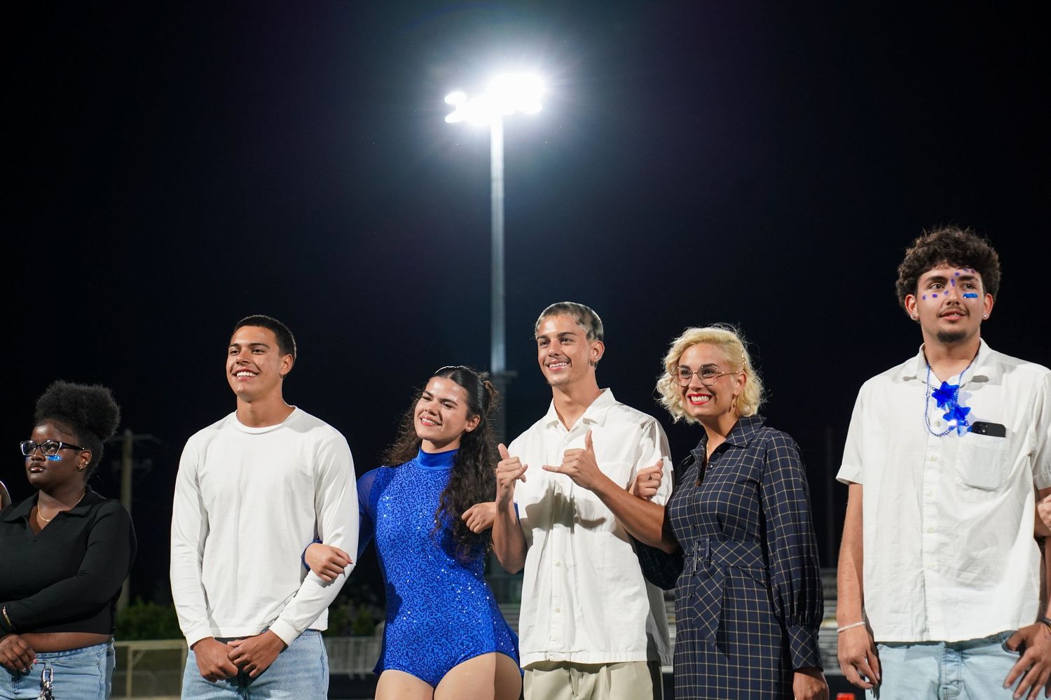 Students standing in line under bright stadium lights during a nighttime event.