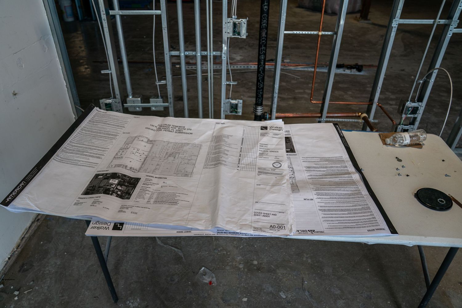 Construction site interior showing metal framing and building plans laid out on tables.