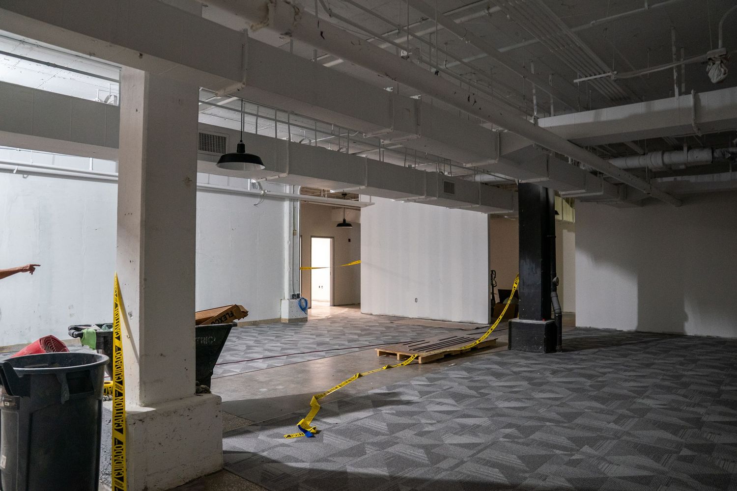 Large commercial area undergoing renovation with carpeted floors and exposed ceiling.